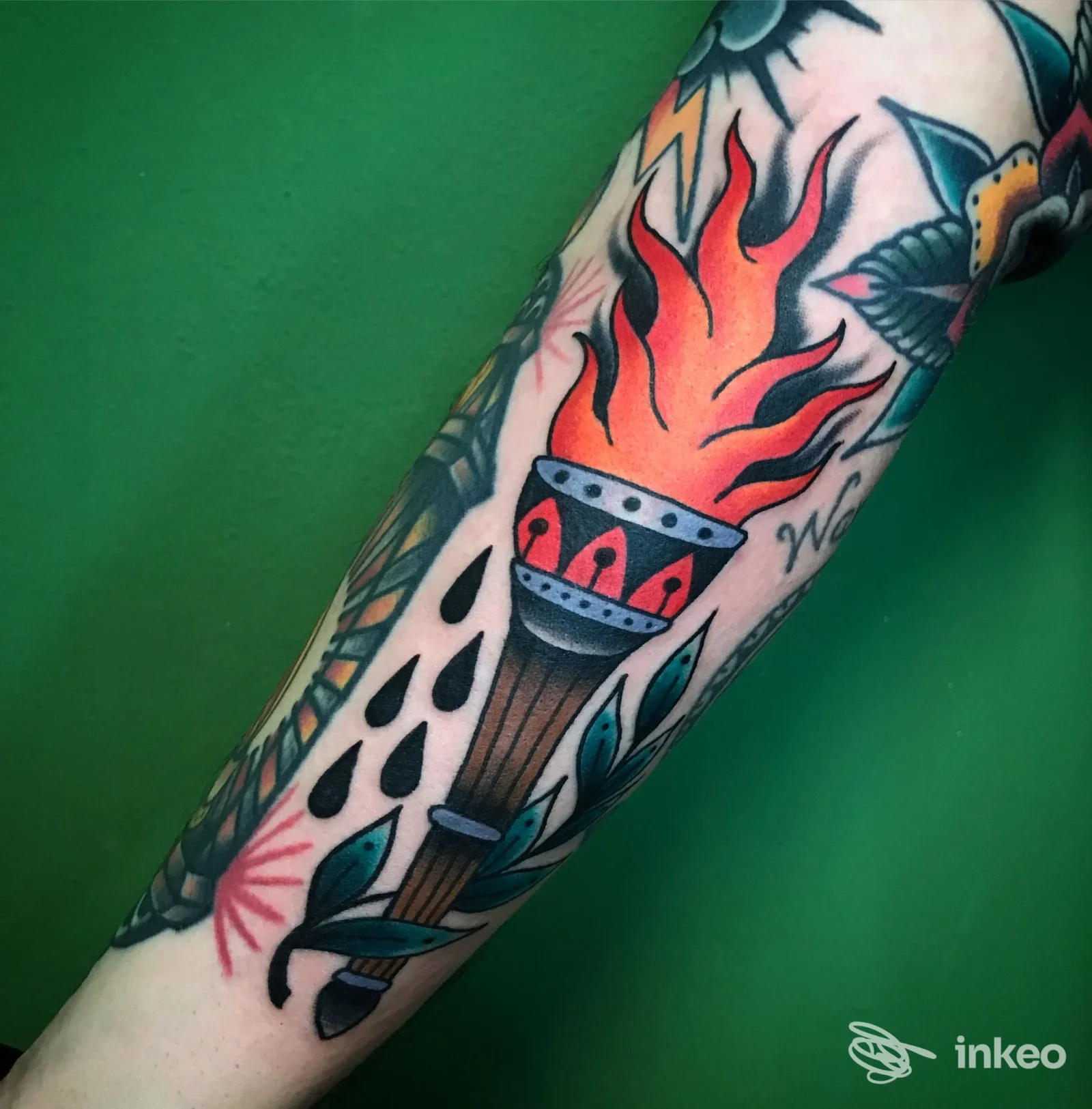 Avambraccio con tatuaggio tradizionale: fiaccola fiammeggiante, gocce nere e foglie stilizzate su pelle chiara, foto per portfolio. RED REAPER TATTOO, Fontane.