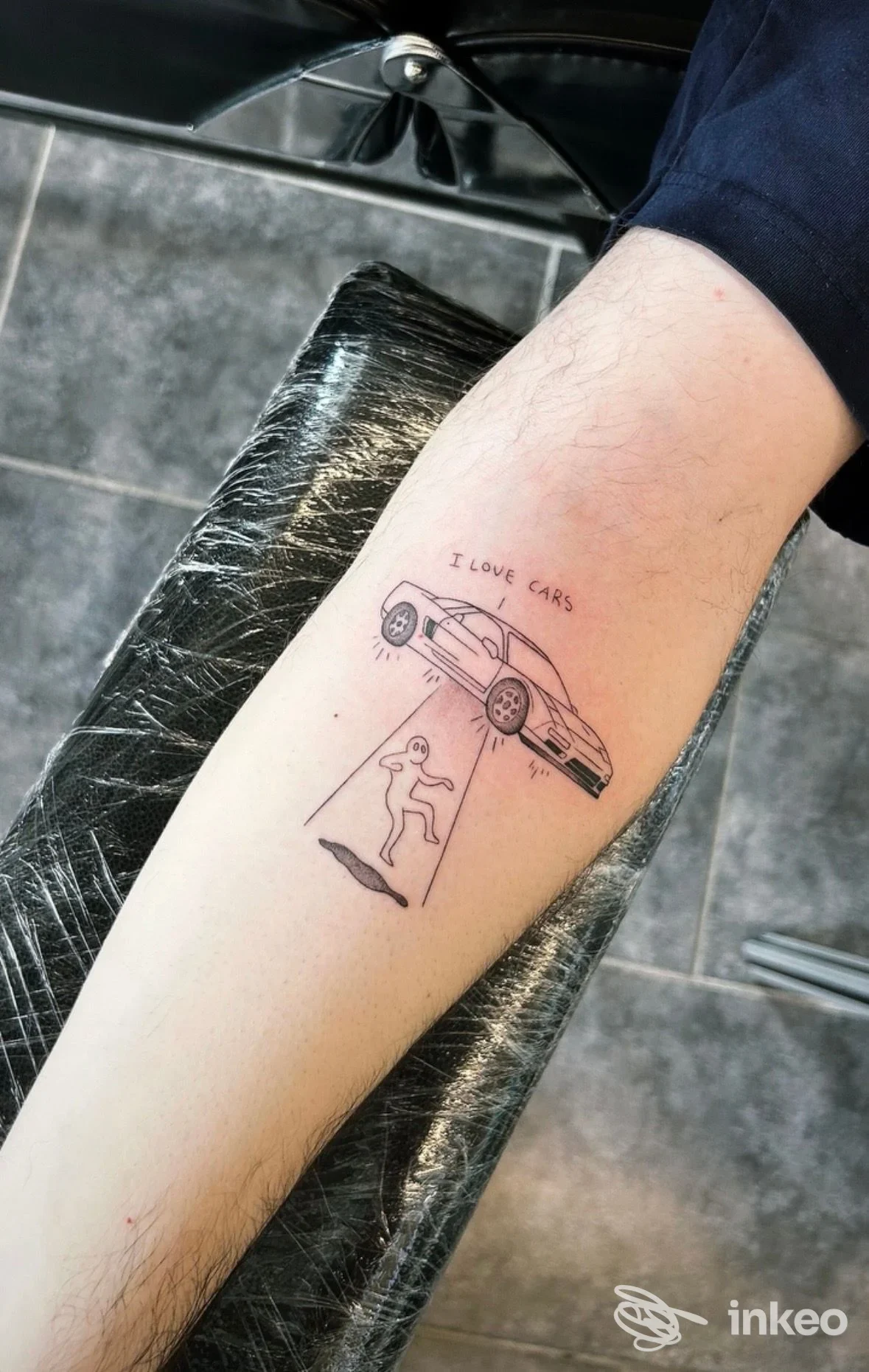 Avambraccio con tatuaggio a linee sottili: un'auto sollevata sopra una figura stilizzata e la scritta I LOVE CARS.
