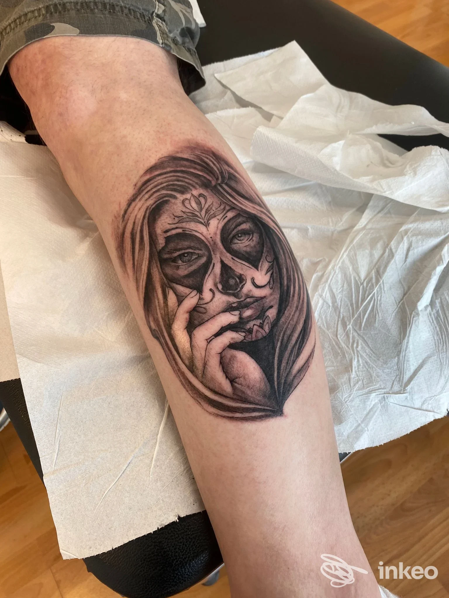 Tatuaggio in bianco e nero di un volto in stile sugar skull con mano sul polpaccio; PuraVida tattoo, Quinto.