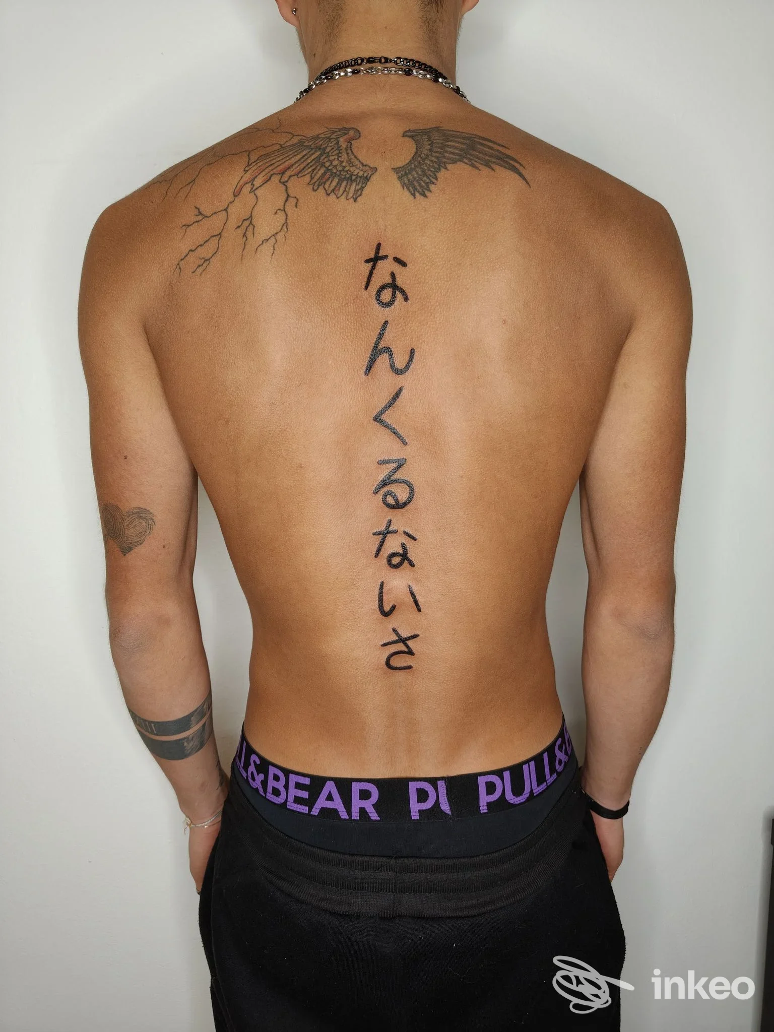 Vista posteriore di un uomo con tatuaggi sulla schiena e scritta giapponese lungo la colonna vertebrale. Foto per Ruvoxa Tattoo, Treviso.