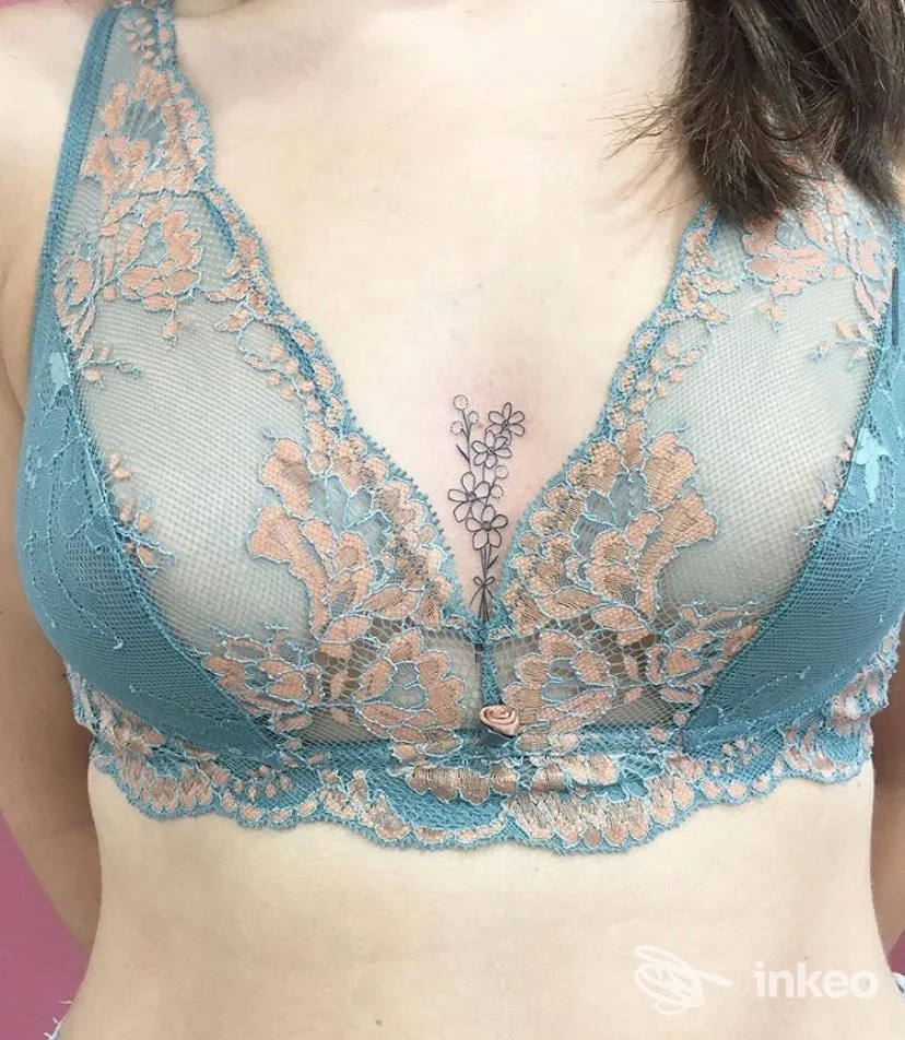 Piccolo tatuaggio floreale sullo sterno tra le coppe di un reggiseno color turchese. Sara Blink Tattoo, Belluno.