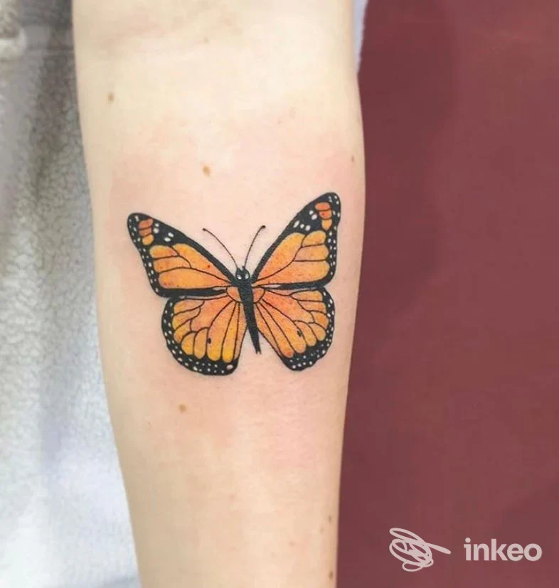 Tatuaggio a forma di farfalla monarca sull'avambraccio, contorni neri e riempitura arancione, realizzato da Sara Blink Tattoo a Belluno.