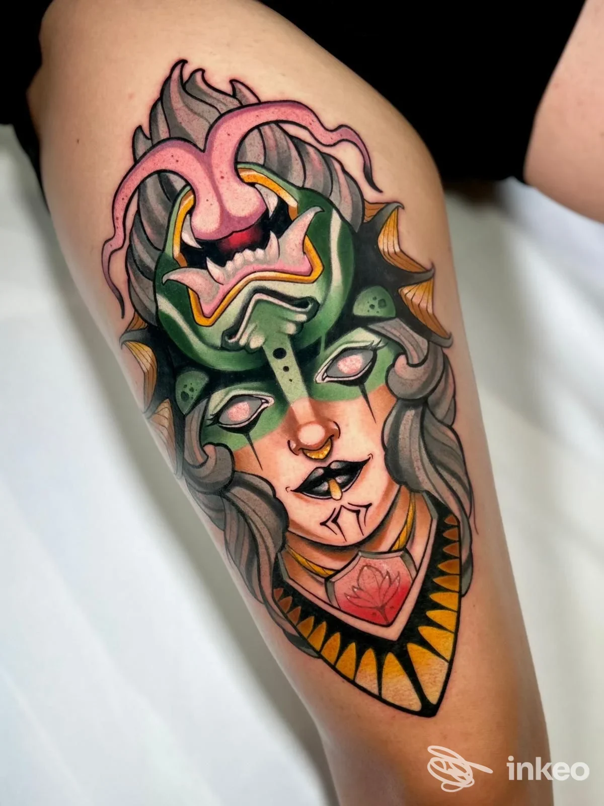Tatuaggio colorato su coscia: volto mascherato con dettagli verdi e rosa, lavoro di Senza tempo tattoo, Stra.
