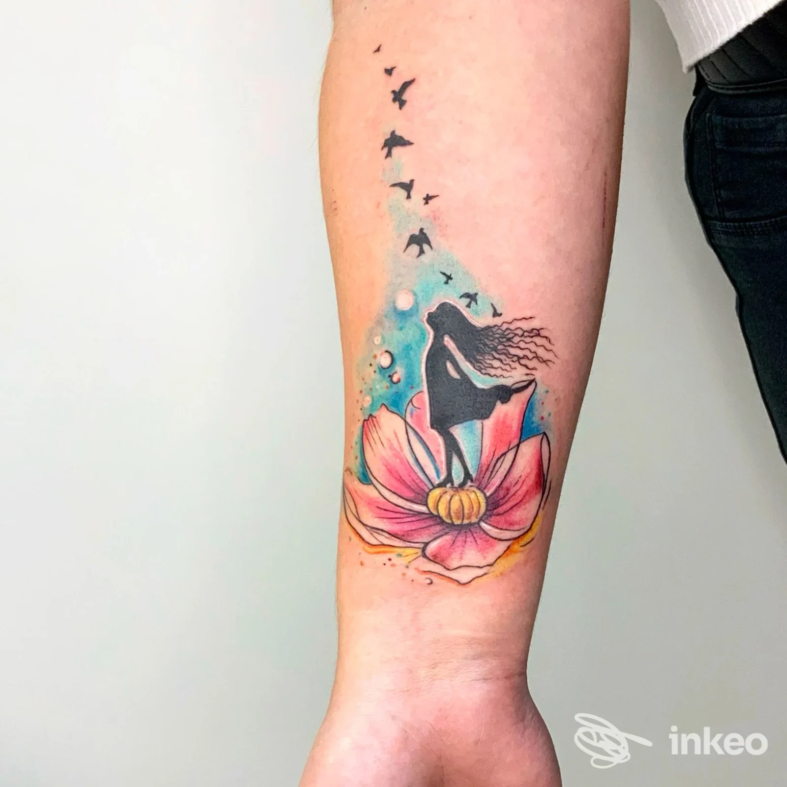 Tatuaggio colorato su avambraccio con fiore rosa e silhouette nera, lavoro di Silvietta Tattoo a Soave, vista frontale del braccio.