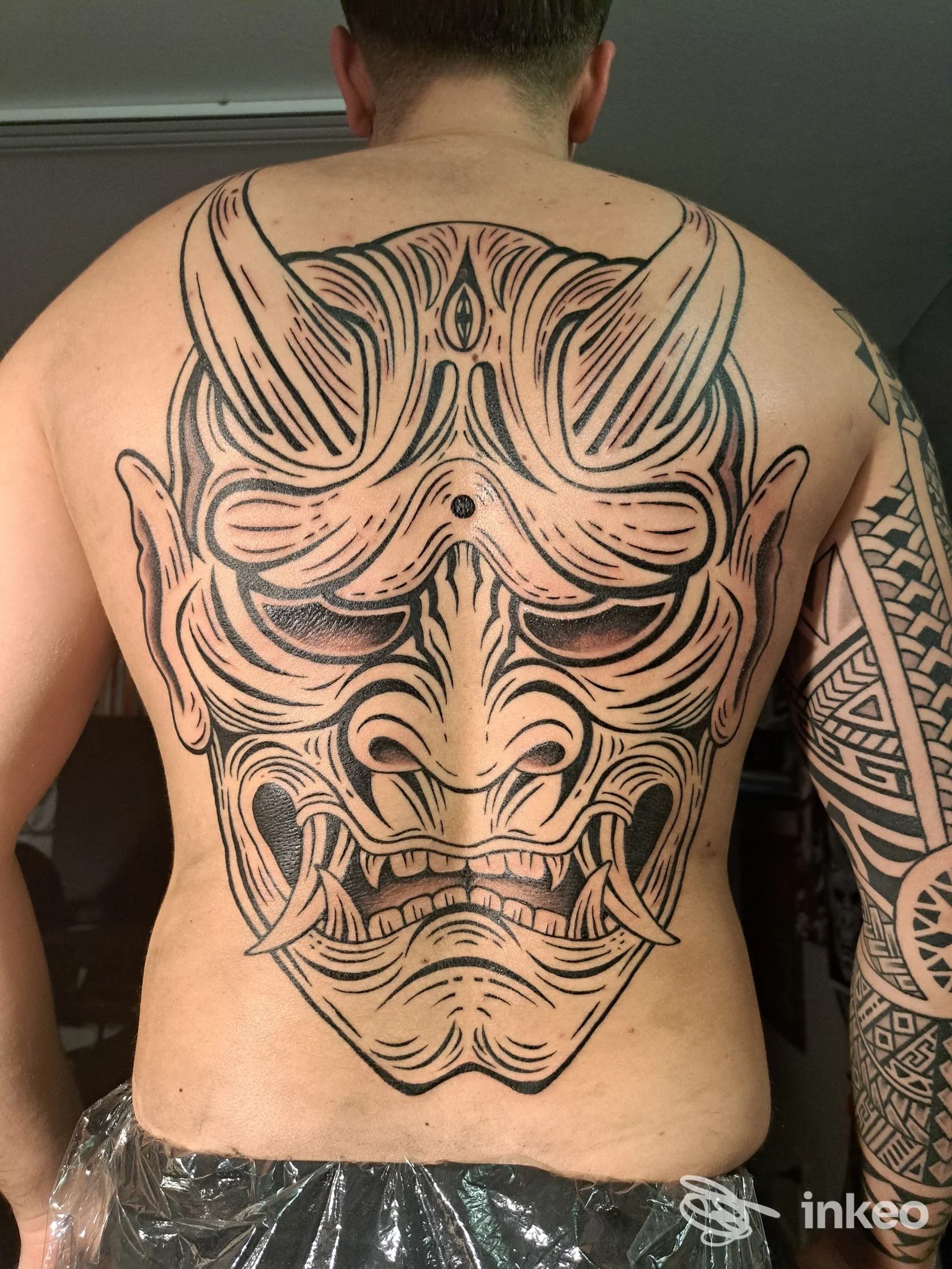 Tattoo visibile sulla schiena di un uomo; disegno grande in stile linework con maschera demoniaca che occupa tutta la schiena, senza testo o elementi promozionali visibili. Studio Black Hole.