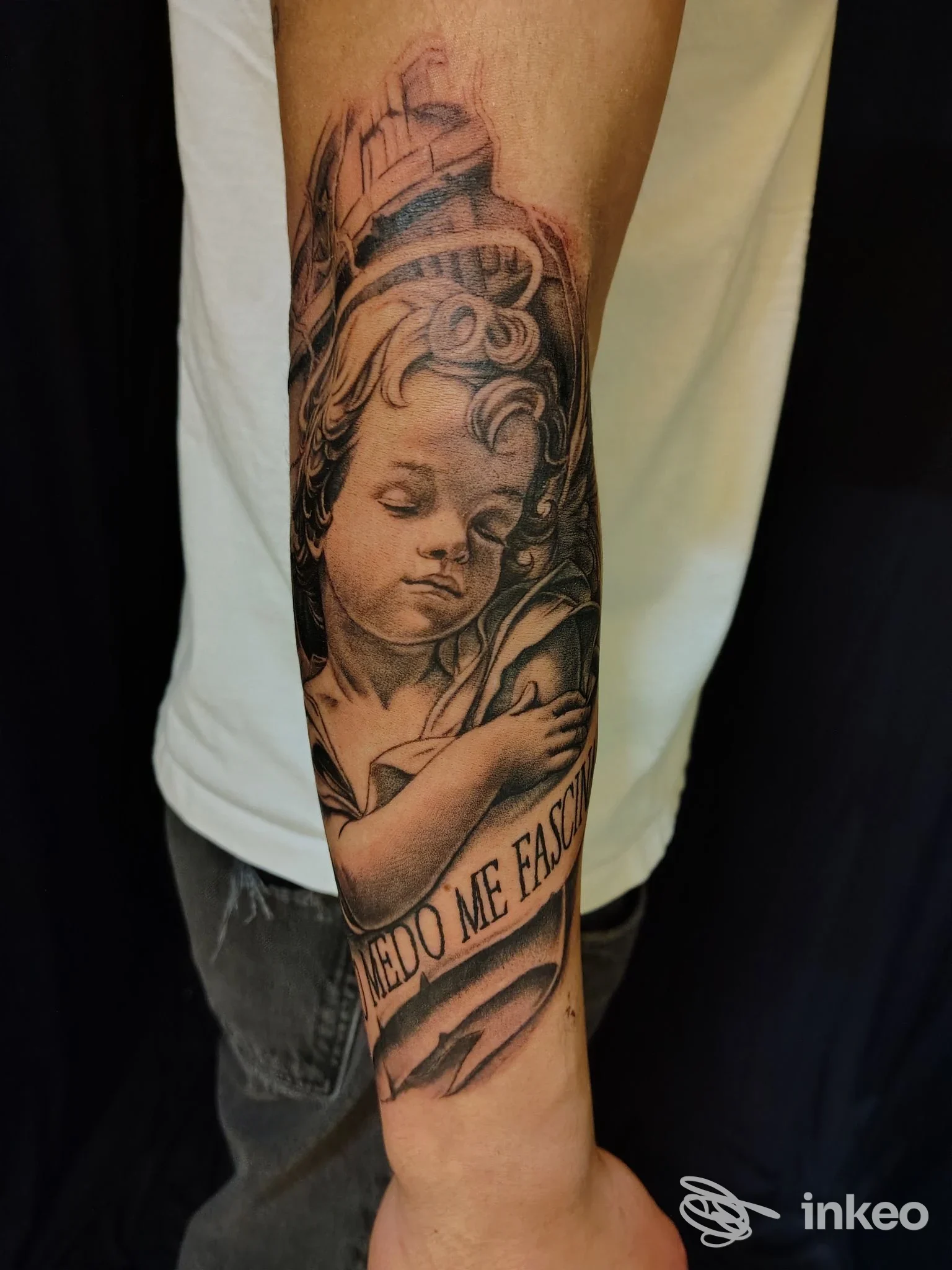Tatuaggio realistico di un putto con una fascia testuale sull'avambraccio, fotografia commerciale del lavoro. Skin up tattoo, Albaredo.