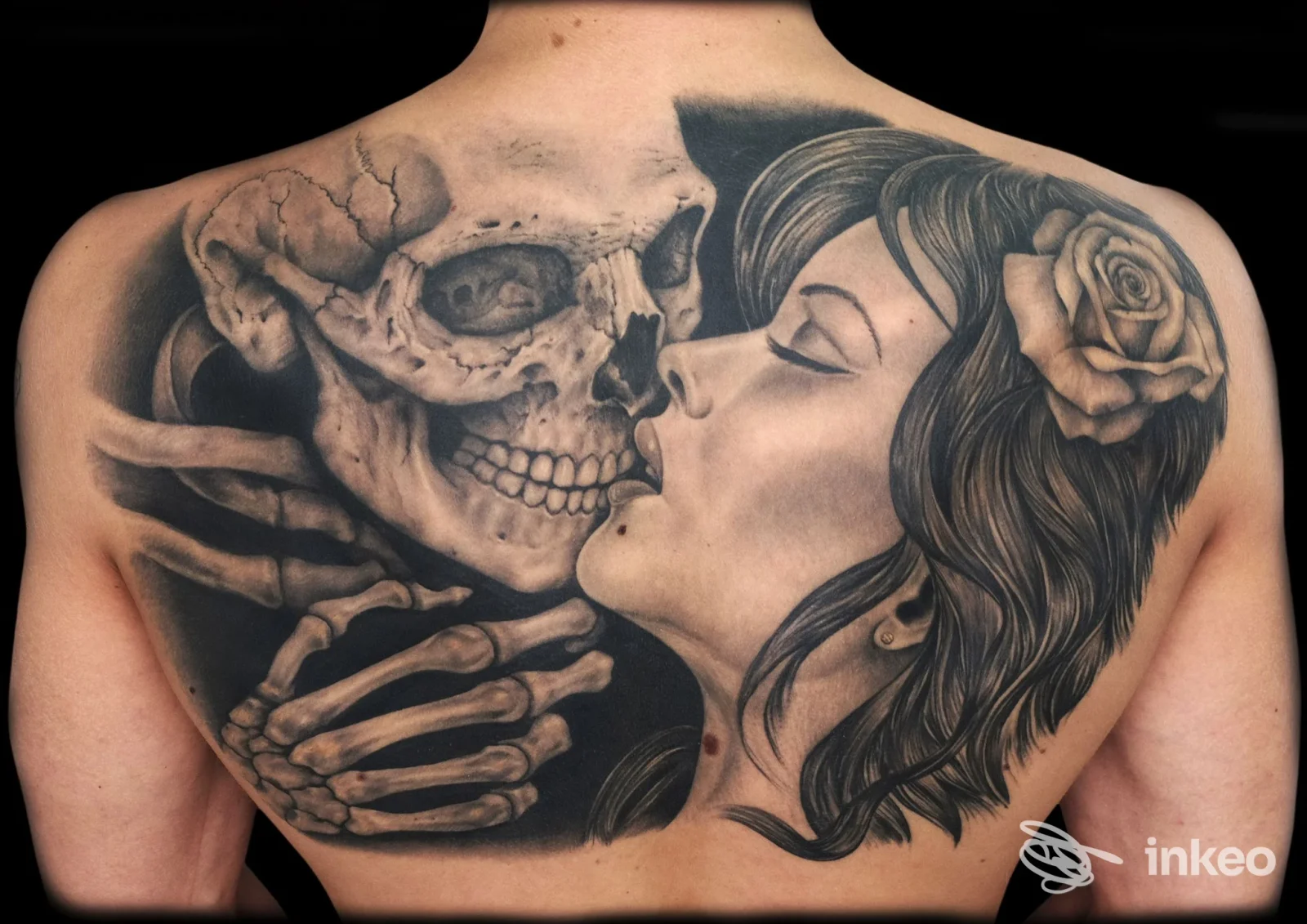 Ampio tatuaggio black & grey sul dorso con un teschio che si avvicina al profilo di una donna con rosa, immagine da Tattoo Consortium, Venezia.