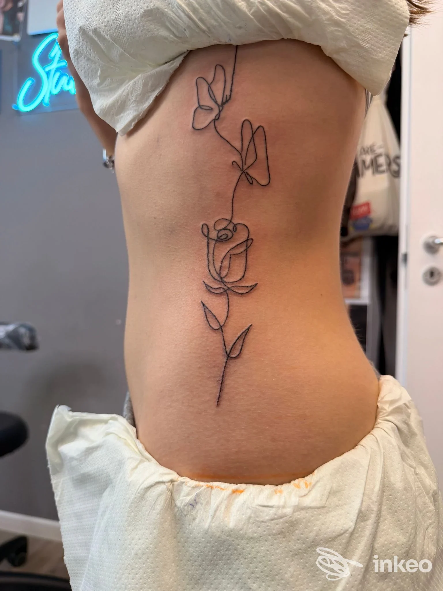 Tatuaggio a linea continua nero raffigurante rose e fiori sul fianco di una persona, lavoro fotografato presso Studio 1106 Tatuaggi e Piercing, Spinea.