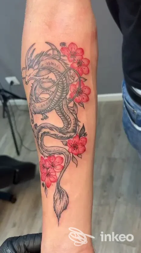 Tatuaggio drago con fiori rosa/rossi sull'avambraccio, realizzato da Studio 1106 Tatuaggi e Piercing a Spinea.