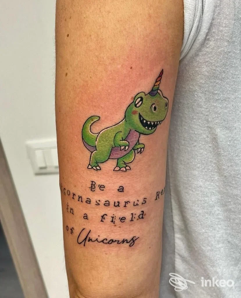 Tatuaggio colorato sull'avambraccio raffigurante un dinosauro-unicorno e scritte sottostanti, foto inviata da Tattoo Utopia, Verona.