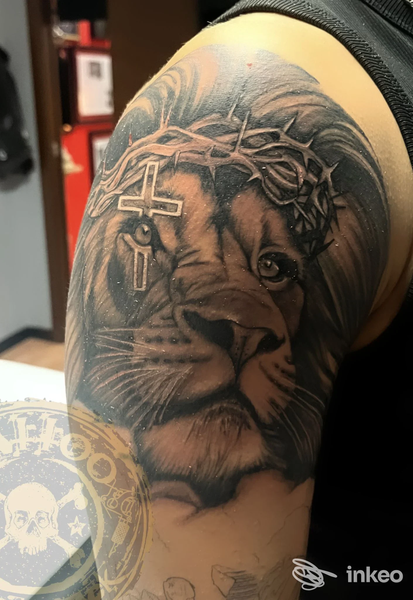 Grande tatuaggio realistico in bianco e nero di un leone con corona di spine e croce sul bicipite, lavoro realizzato presso Black Jack tattoo studio, Verona.