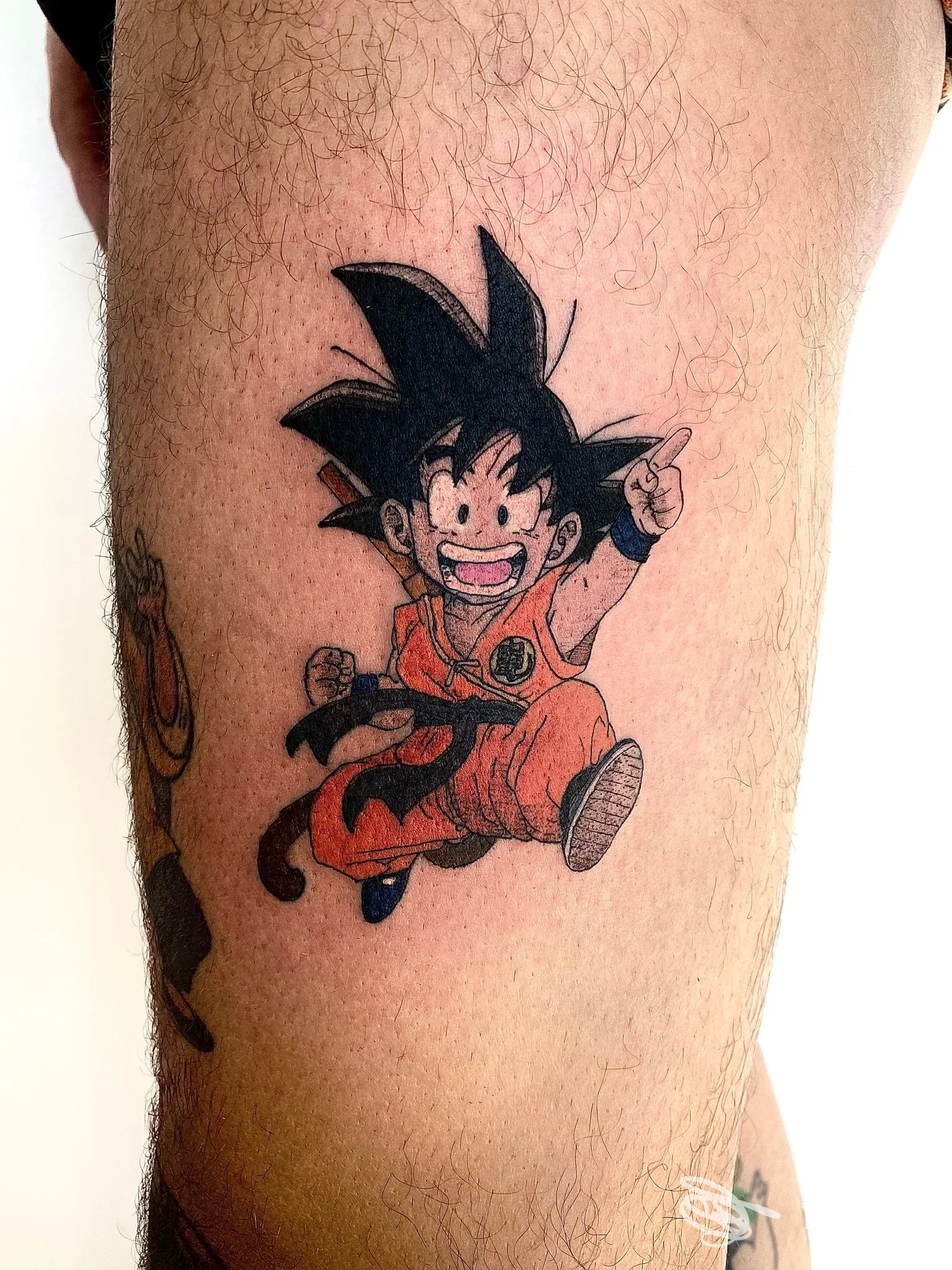Tatuaggio a colori raffigurante Goku in stile cartoon su coscia, fotografato per Black Sweat Tattoo Studio a Cerea.