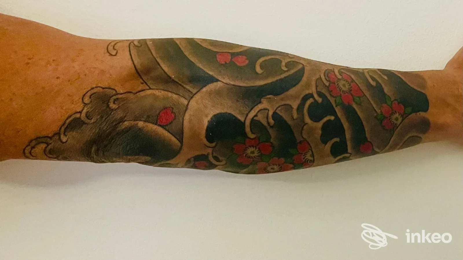 Avambraccio tatuato con grandi aree scure e fiori rossi, foto di Adrenalink Tattooing, Quinto.