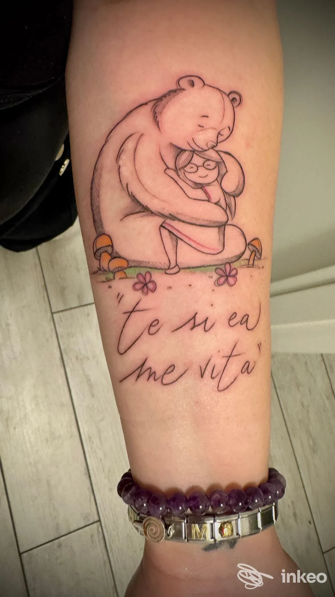 Tatuaggio sull'avambraccio raffigurante un orso che abbraccia una bambina con scritta corsiva sotto. Billion Dollar Tattoo, Candiana.