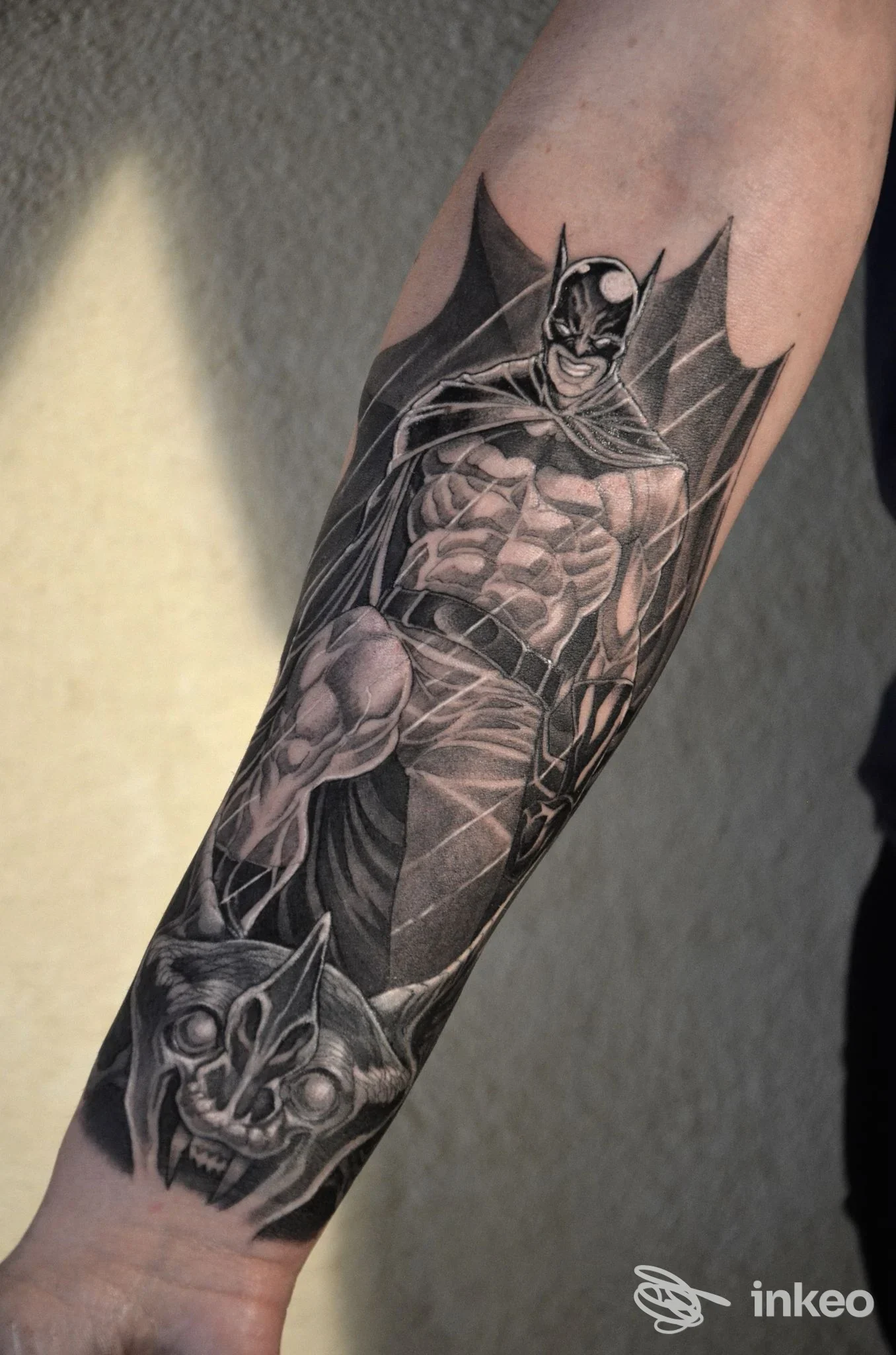 Tatuaggio in bianco e nero di Batman su avambraccio, con texture e contrasti marcati, visibile in enfatizzato.