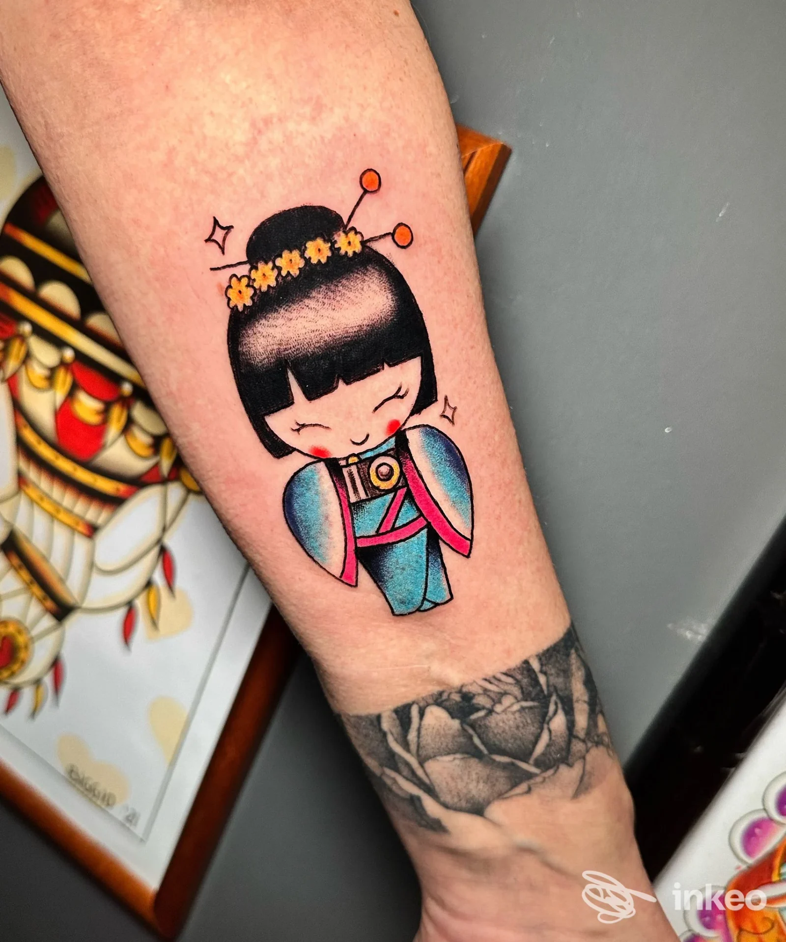Tatuaggio colorato di una bambolina/kokeshi sull'avambraccio, realizzato da Bunkerino Tattoo Shop a Venezia.