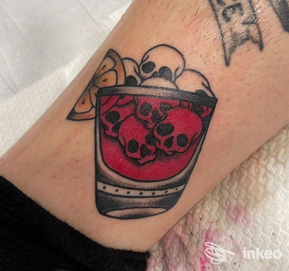 Tatuaggio colorato su braccio raffigurante un bicchiere con liquido rosso e teschi, immagine per Cicatrici d'Inchiostro Walk-In Tattoo Studio, Verona.