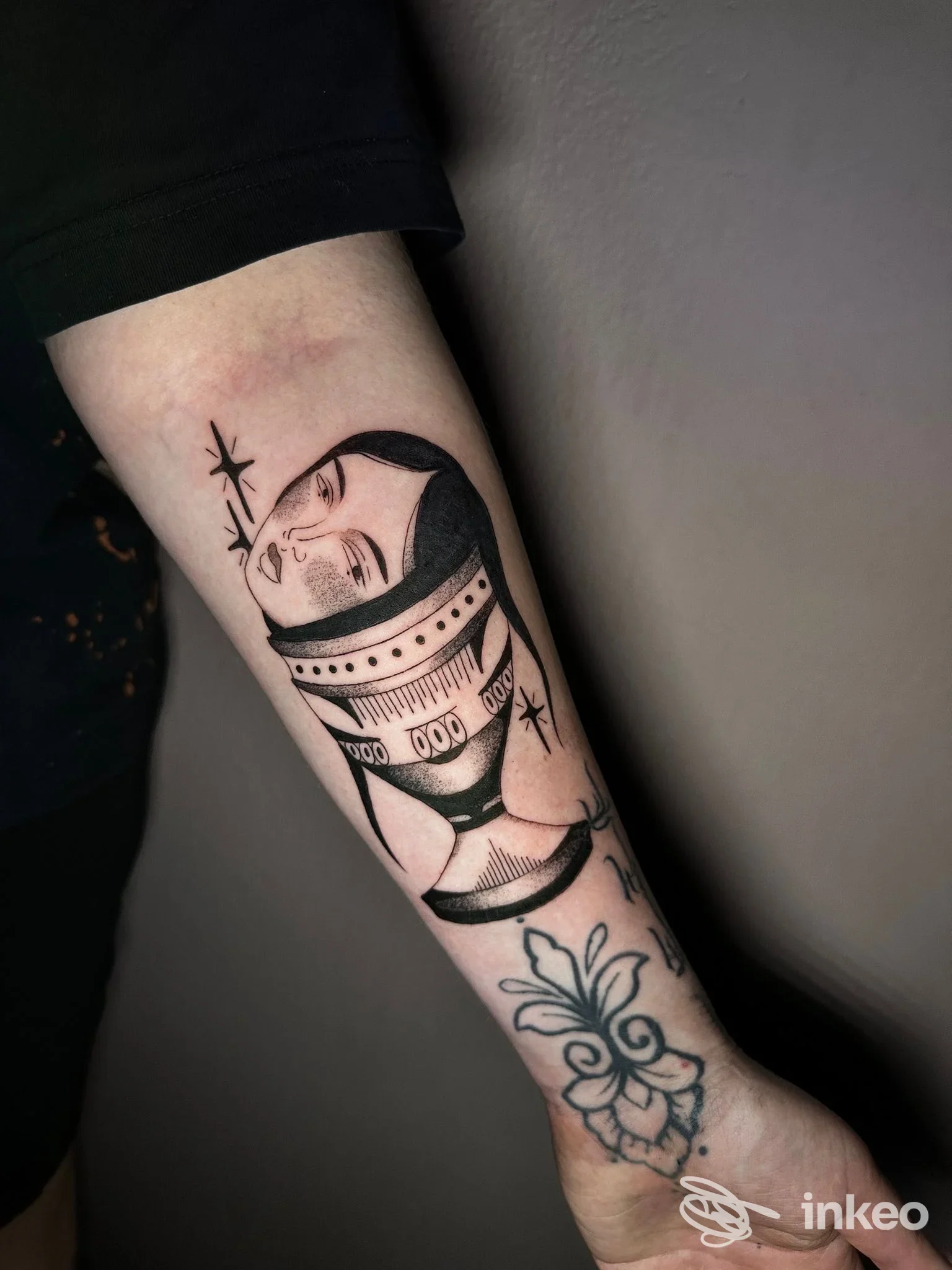 Tatuaggio in bianco e nero sul lato dell'avambraccio raffigurante un volto stilizzato; immagine fornita da Ellie tattoo, Castel d'Azzano.