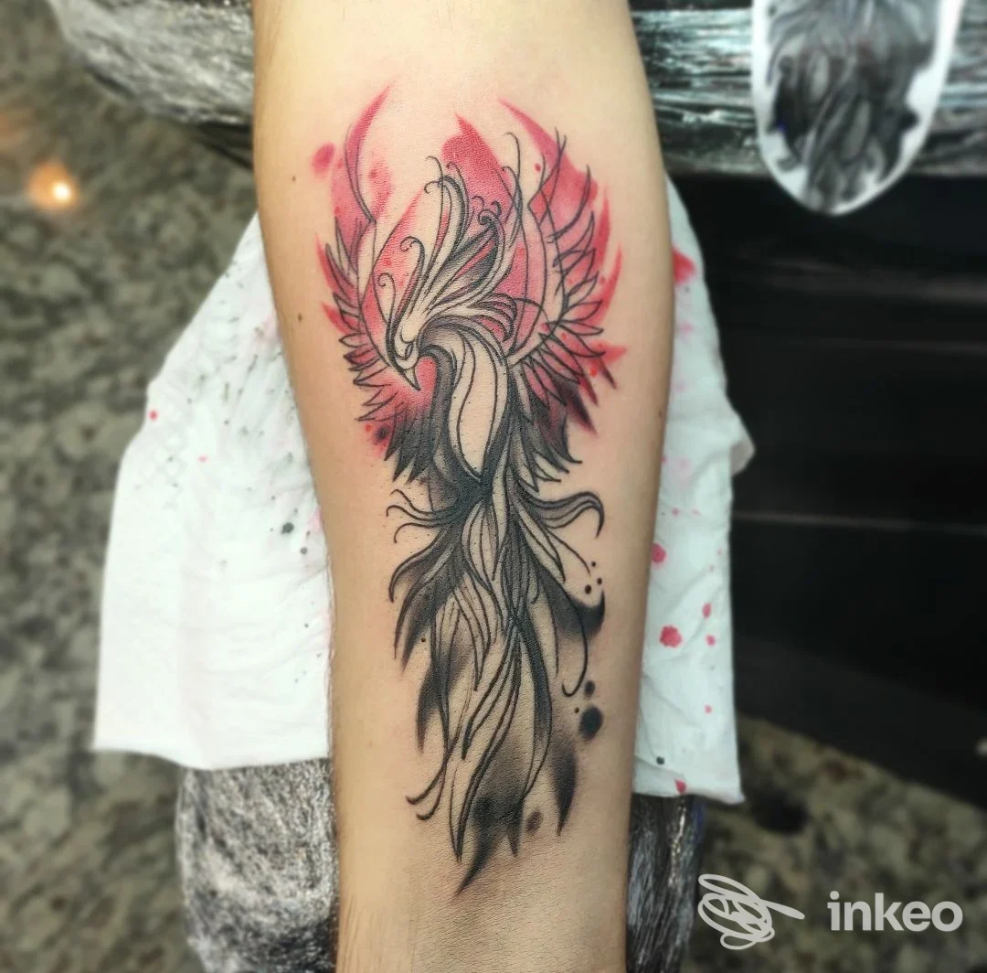 Tatuaggio fenice stilizzata su avambraccio con inchiostro nero e schizzi rossi, Bruce Tattoo Ink Studio Mirano.
