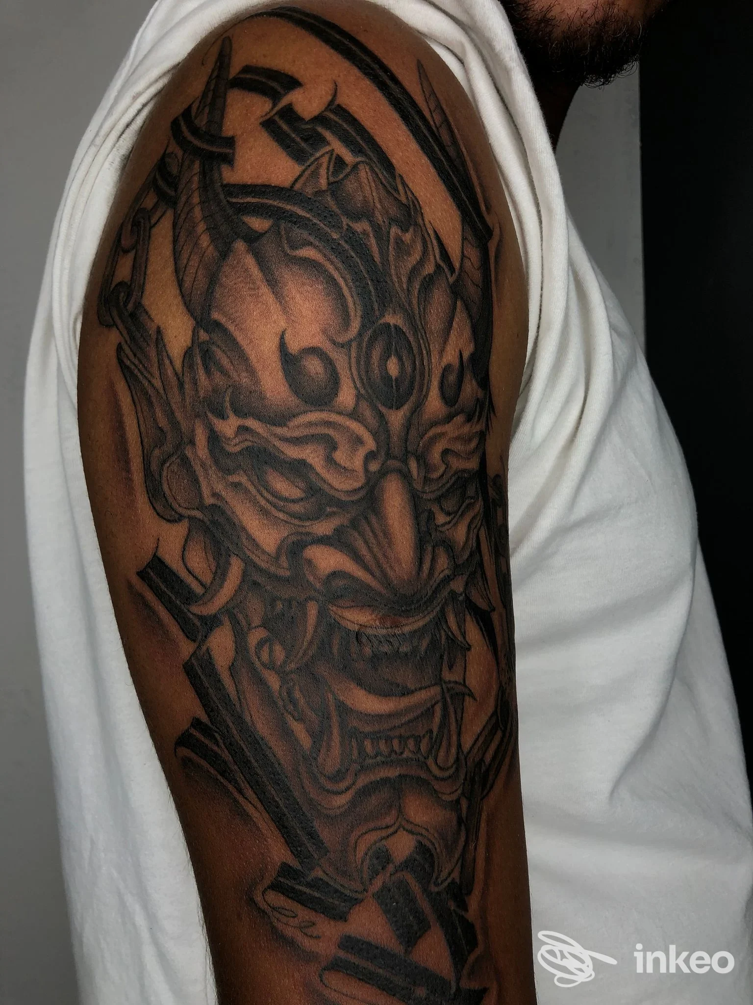 Ampia manica nera/grigio su braccio superiore con maschera demoniaca, foto fornita da Hold Fast Tattoo, Verona.