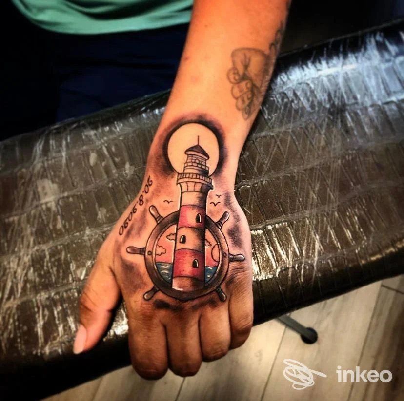 Tatuaggio colorato sul dorso della mano raffigurante un faro inscritto in un timone, foto per portfolio di GELA In-k TATTOO STUDIO, Verona.