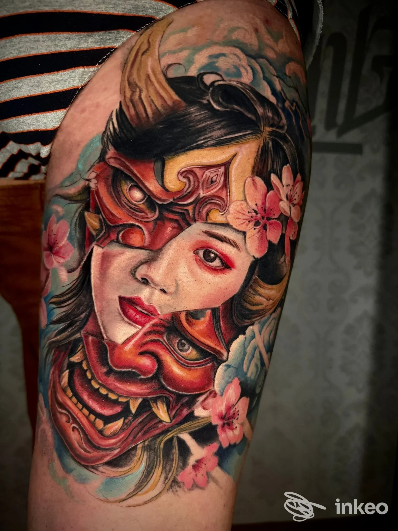 Tatuaggio a colori su braccio superiore raffigurante volto maschera demoniaca e fiori — InKing Tattoo, Caldogno.
