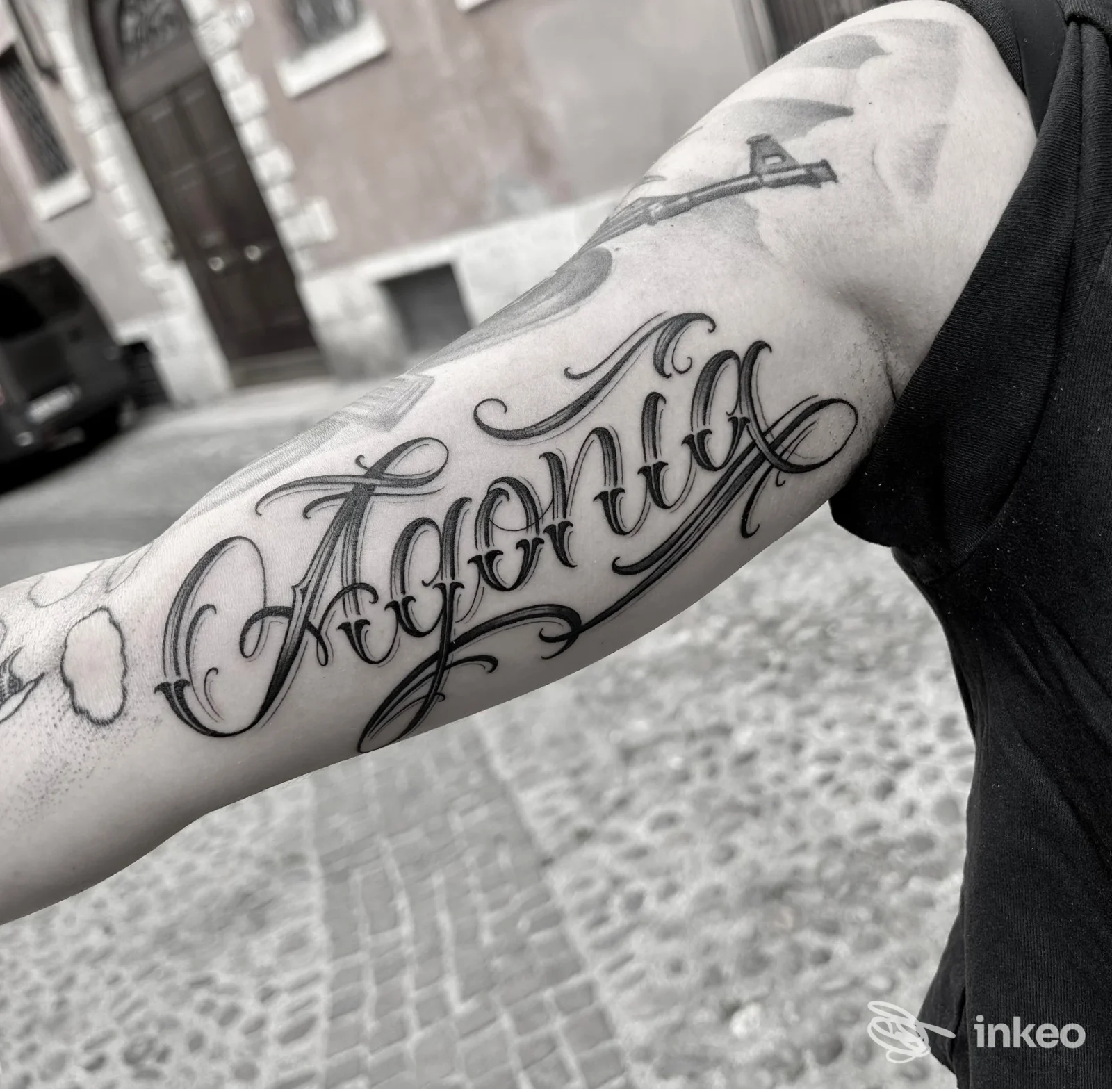 Tatuaggio calligrafico nero sull'avambraccio, fotografia scattata in esterno; Ink Addiction Tattoo Shop, Verona.