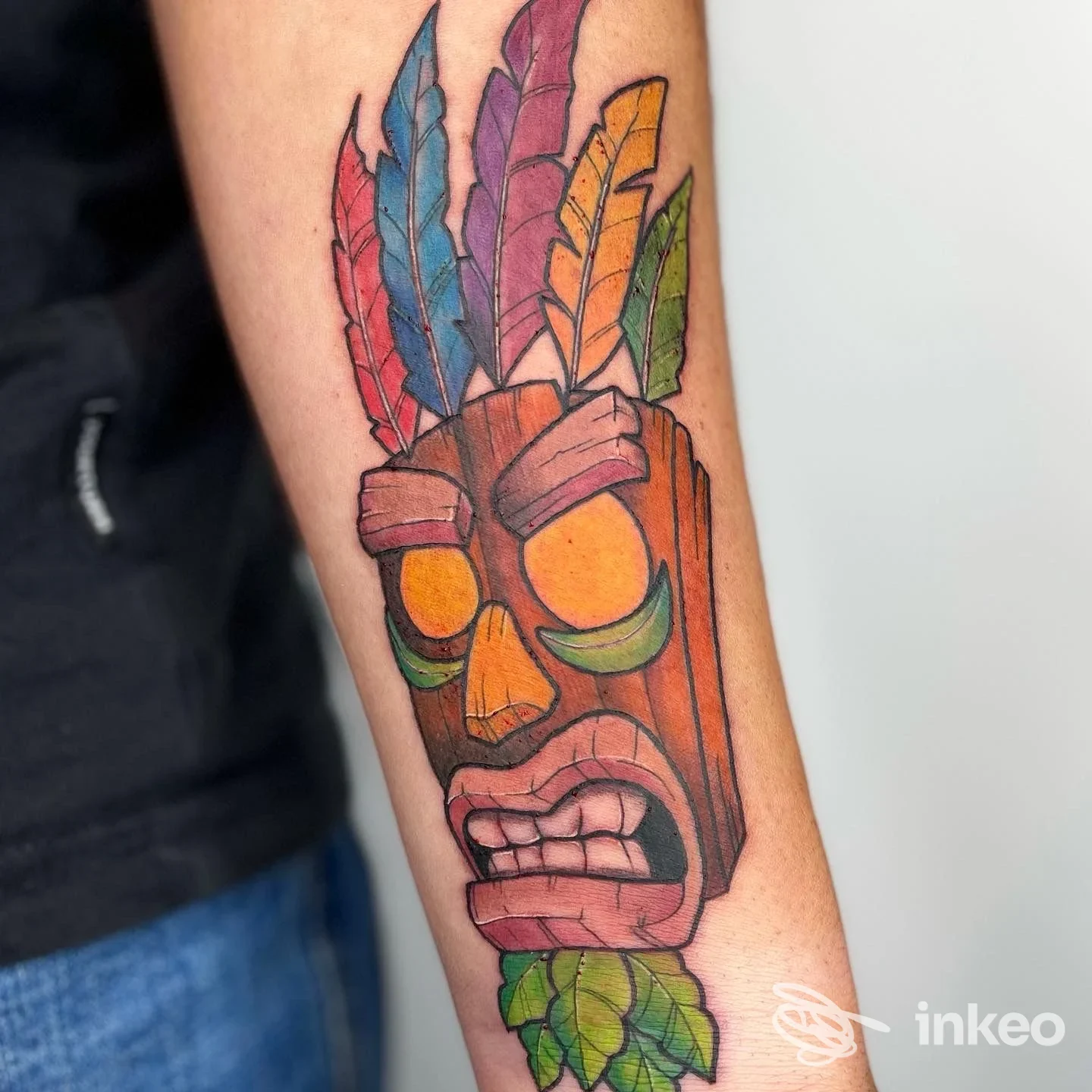 Tatuaggio colorato a forma di maschera/totem con piume sull'avambraccio, La Bottega dei Ghirigori - Tattoo Studio, San Vito di Cadore.
