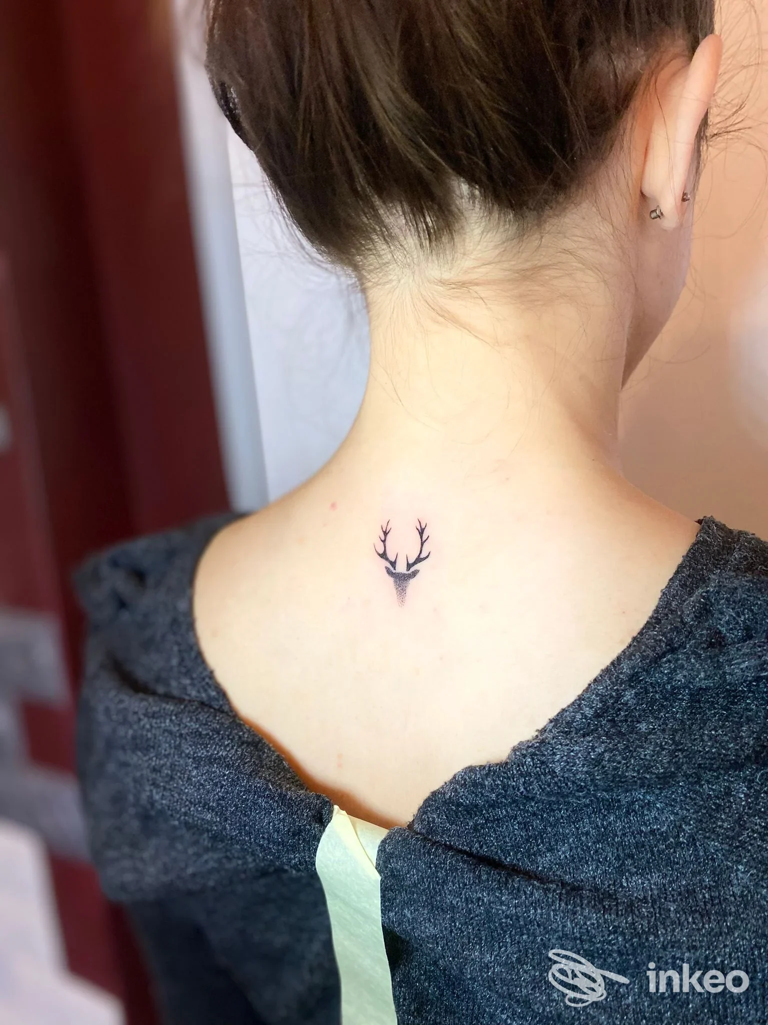 Piccolo tatuaggio nero a forma di testa di cervo sulla nuca di una persona, foto inviata da La Bottega dei Ghirigori - Tattoo Studio, San Vito di Cadore.