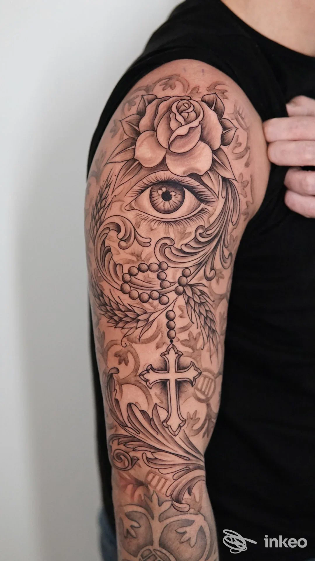 Ampia manica tatuata in stile black and grey con occhio centrale, rose, rosario e croce, fotografata sul braccio. La Corte dei Miracoli Tattoo & Piercing, Bovolone.