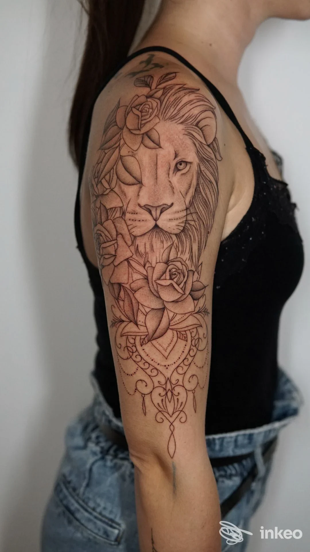Grande tatuaggio su spalla e braccio superiore raffigurante un leone circondato da rose e motivi ornamentali, foto di La Corte dei Miracoli Tattoo & Piercing a Bovolone.