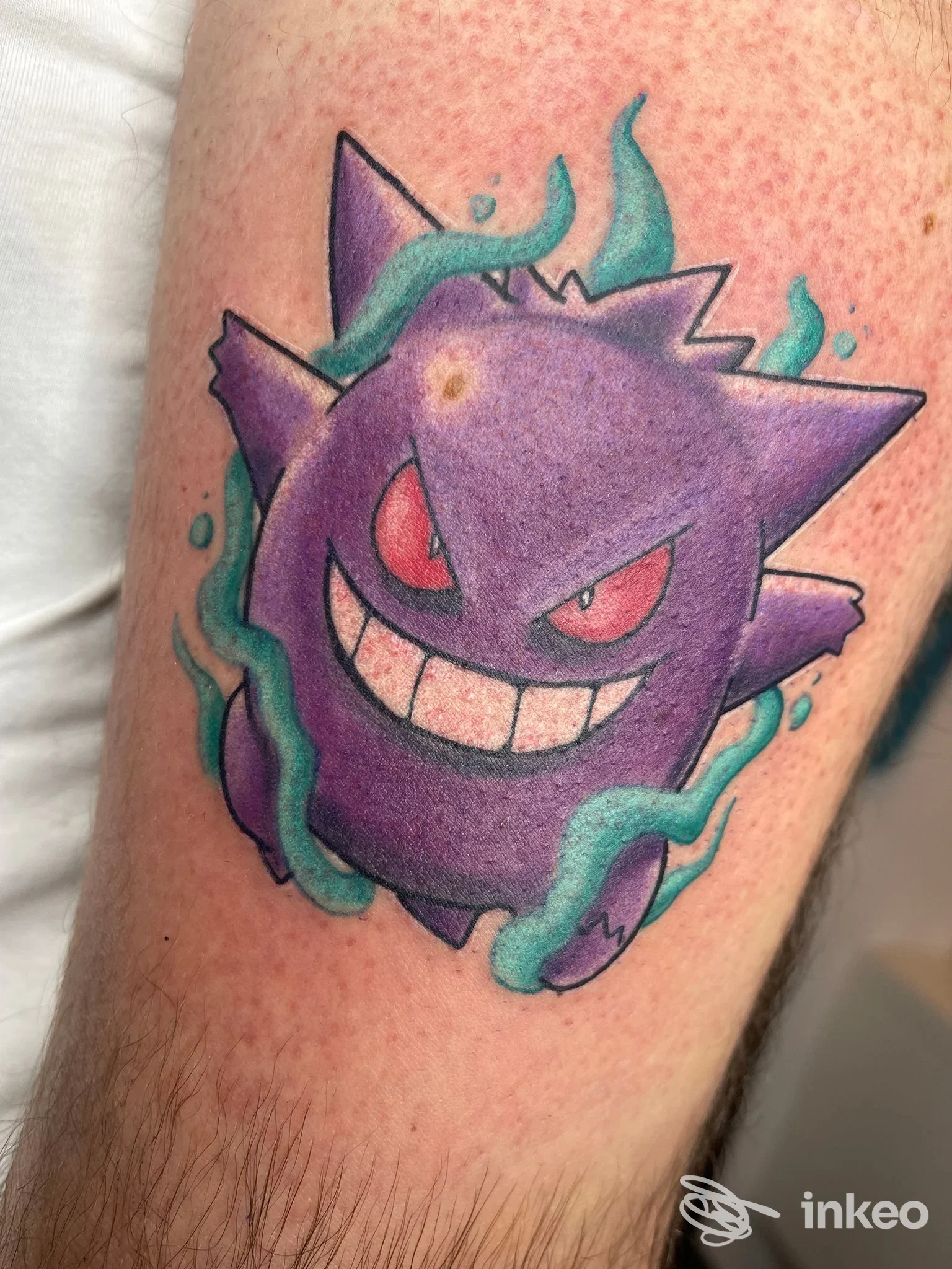Tatuaggio a colori raffigurante Gengar su avambraccio, con ombreggiature viola e dettagli verde acqua, realizzato da Le Maxim - Tattoo Studio a Castelfranco Veneto.