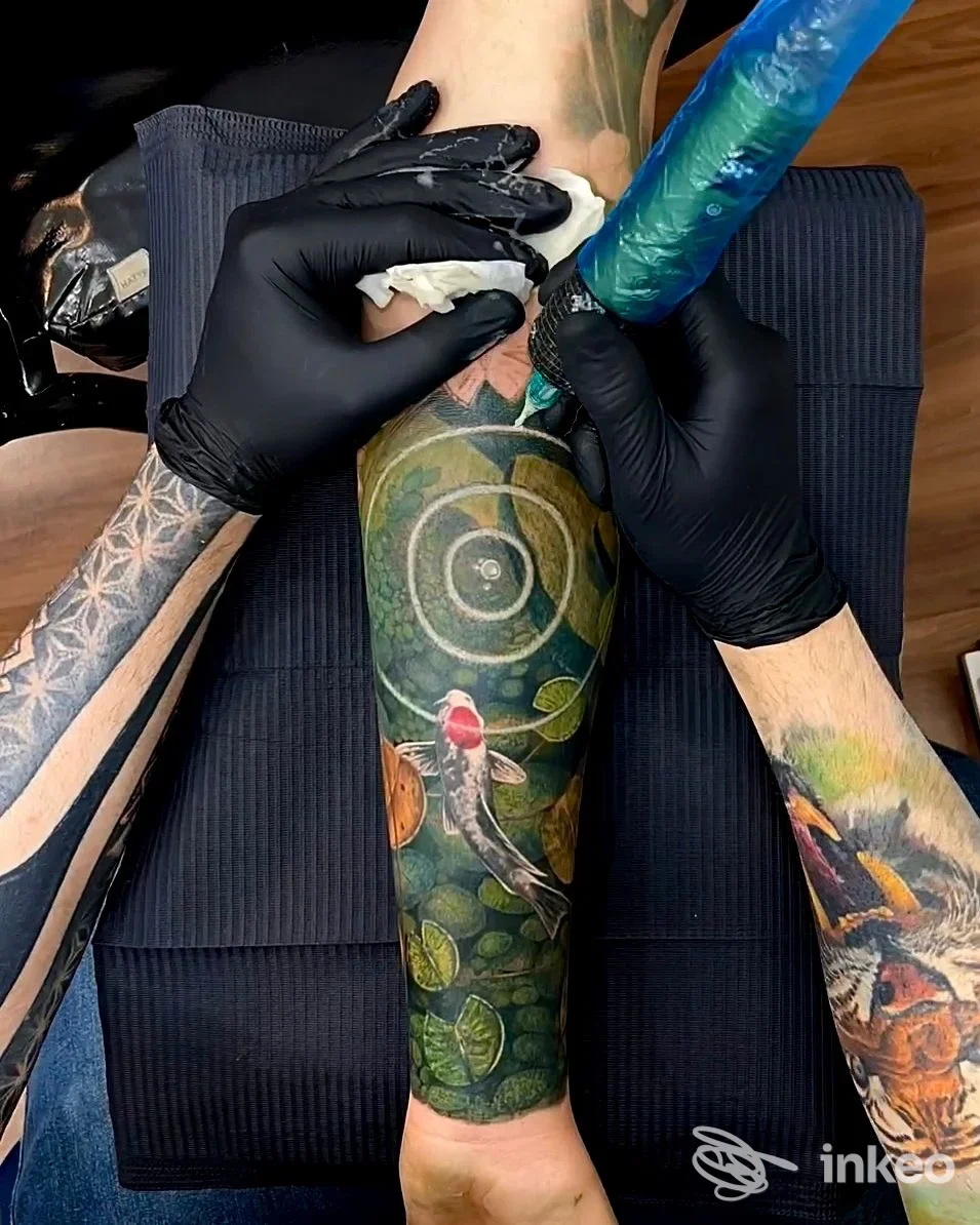 Primo piano di tatuaggio a colori in esecuzione sull'avambraccio, artista al lavoro. Little Tattoo Verona, Verona.