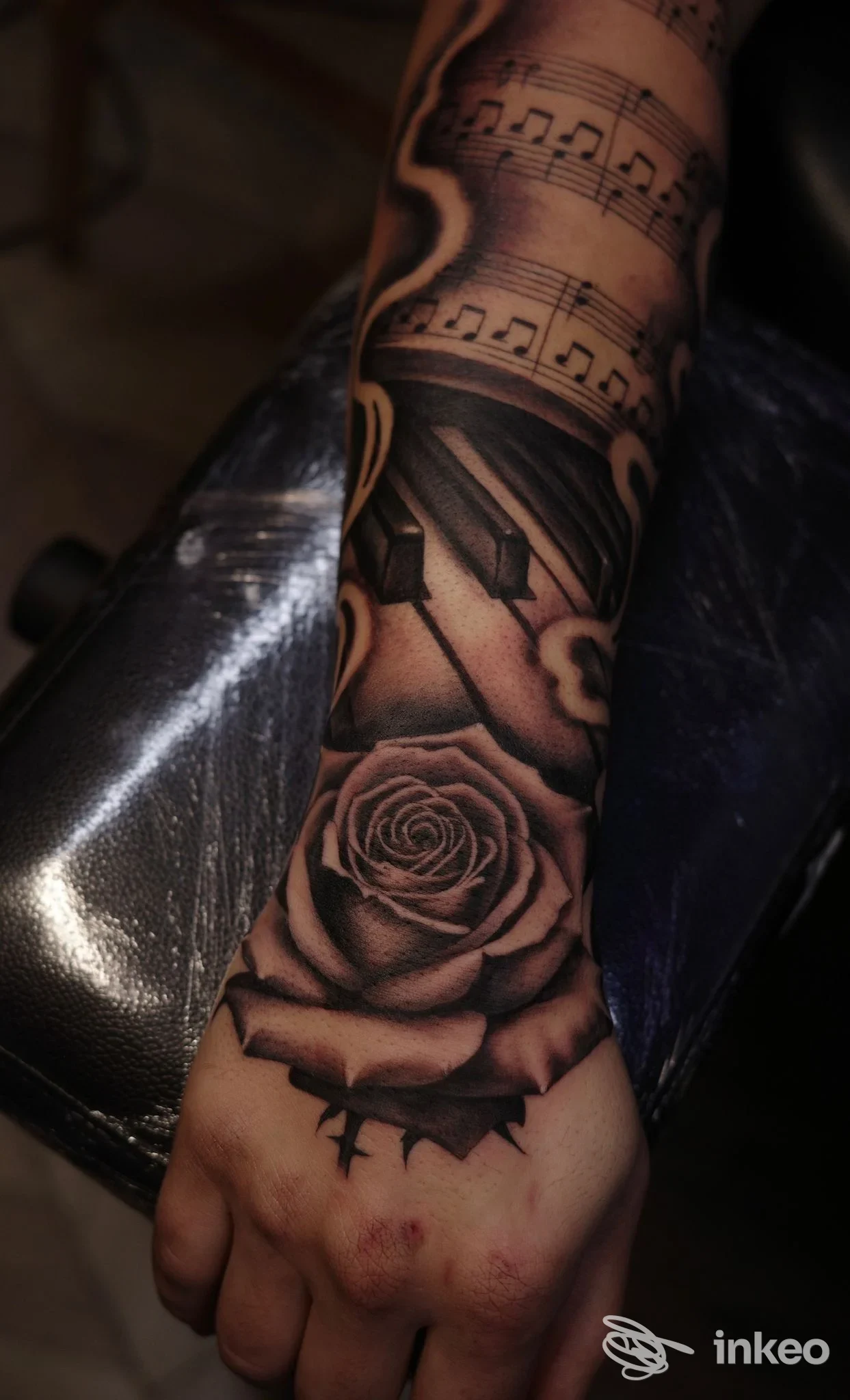 Tatuaggio black & grey su avambraccio e dorso mano con rosa, tasti di pianoforte e spartito — Ninetyfour Tattoo Shop, Verona.
