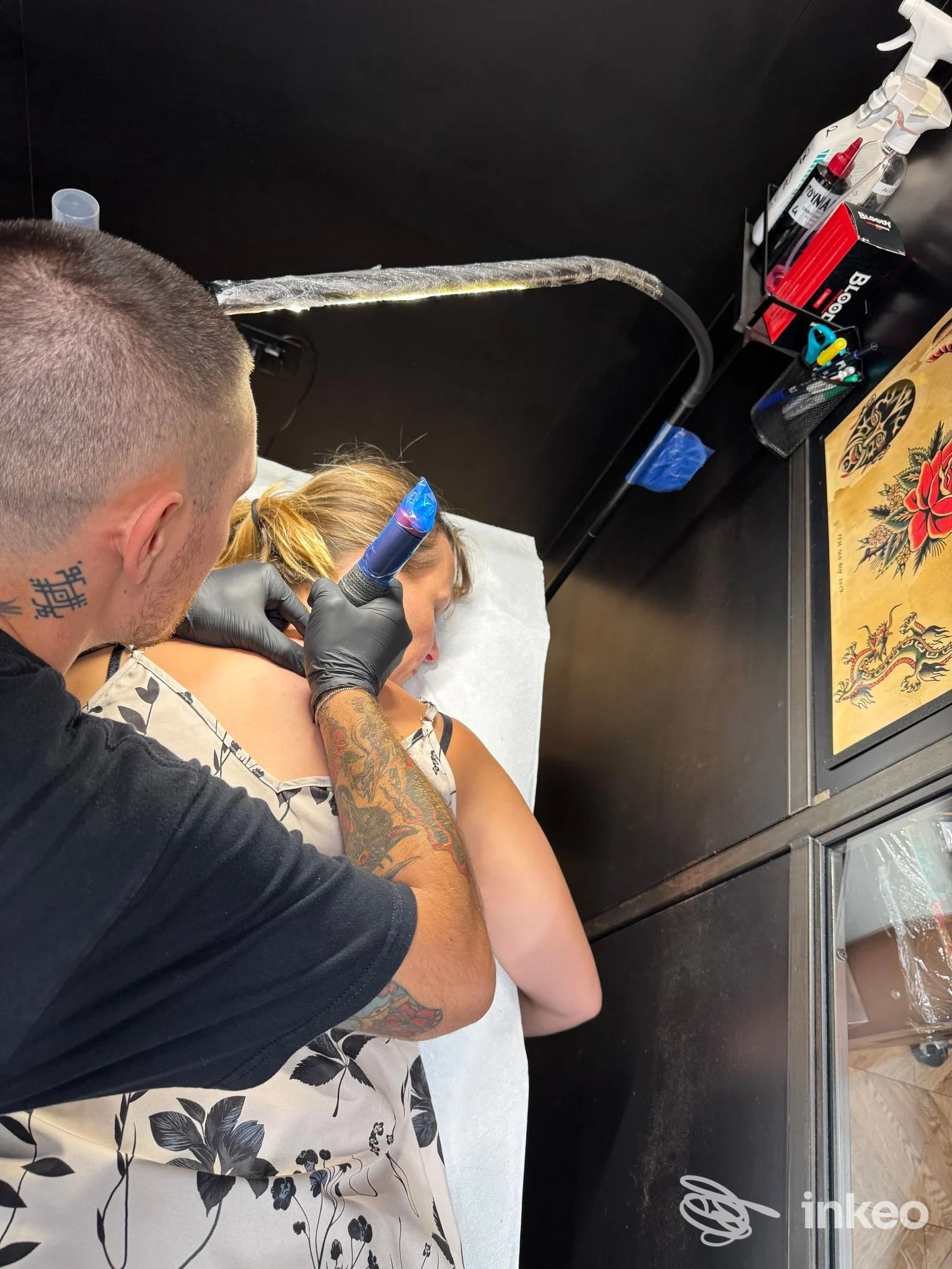 Tatuatore al lavoro sulla parte superiore della schiena/spalla di una cliente nello studio Ninetyfour Tattoo Shop, Verona.