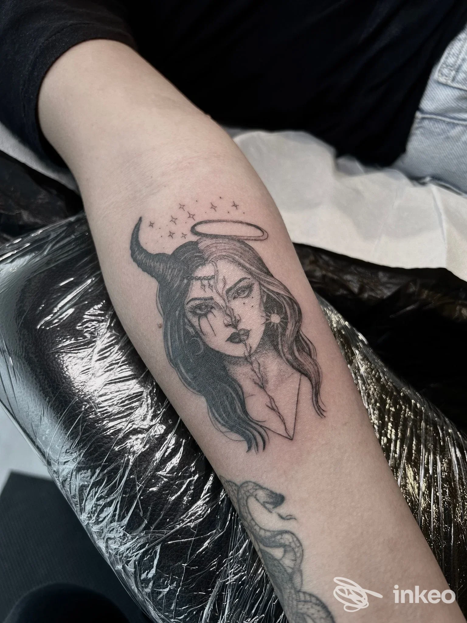 Tatuaggio in bianco e nero raffigurante un volto metà angelo metà demone con alone e corno sull'avambraccio; fotografia relativa a Oldline Tattoo Studio, Sandrigo.