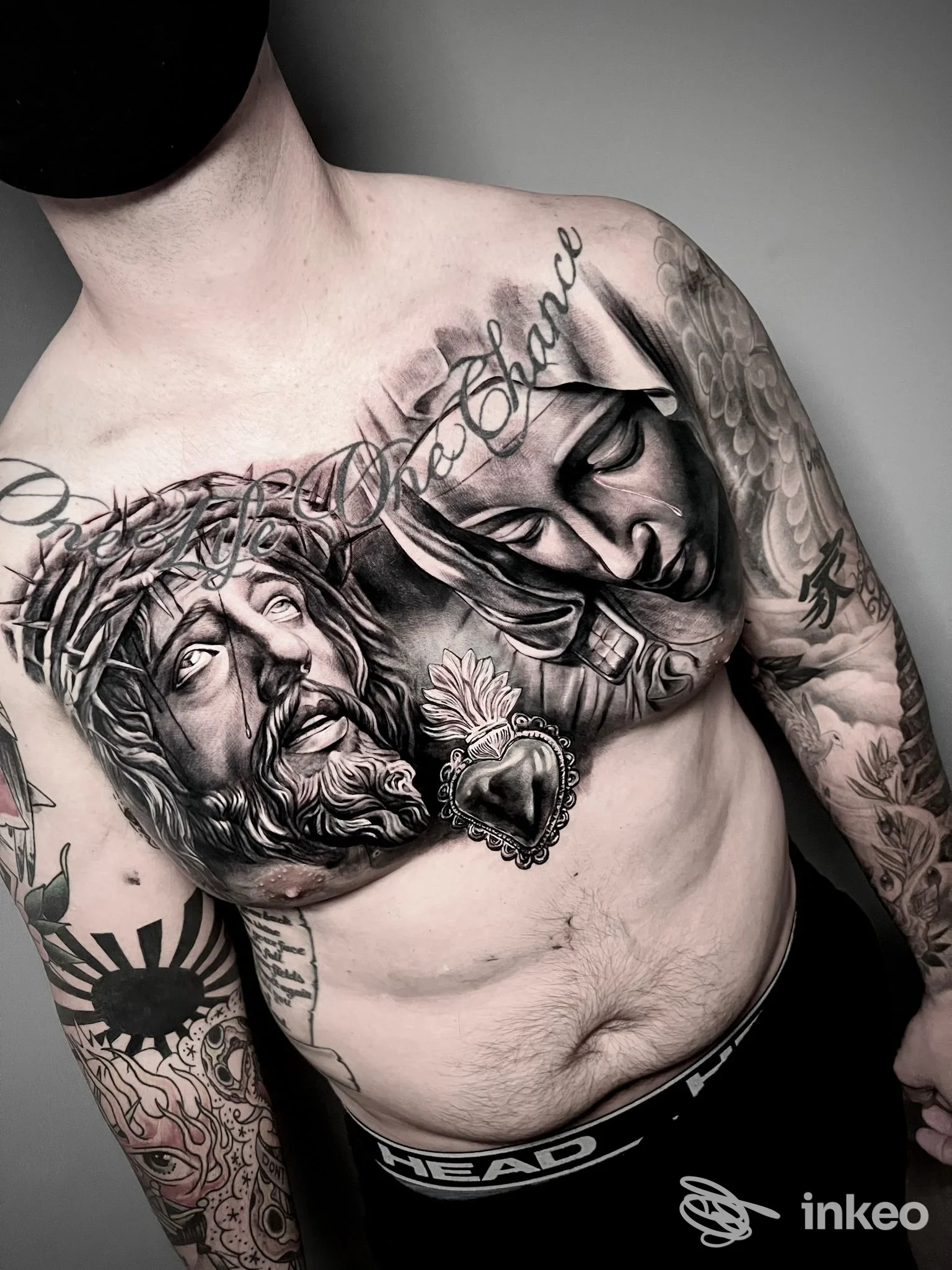 Tatuaggi realistici su petto e braccio di un uomo, ritratti religiosi e cuore sacro. STUDIO MURH TATTOO, Arlesega.