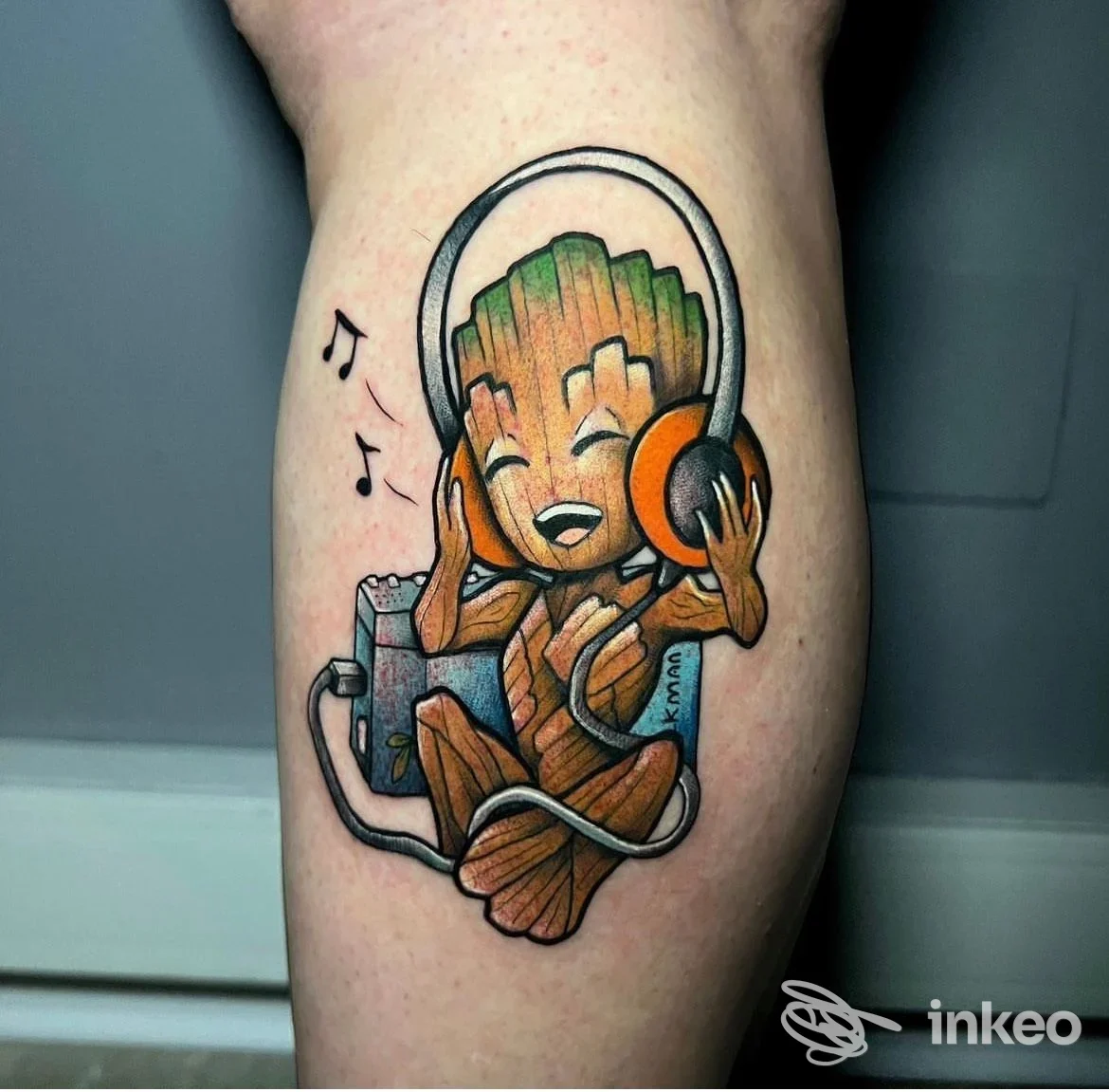 Tatuaggio colorato su polpaccio raffigurante un personaggio tipo Baby Groot con cuffie, lavoro fotografato in primo piano.