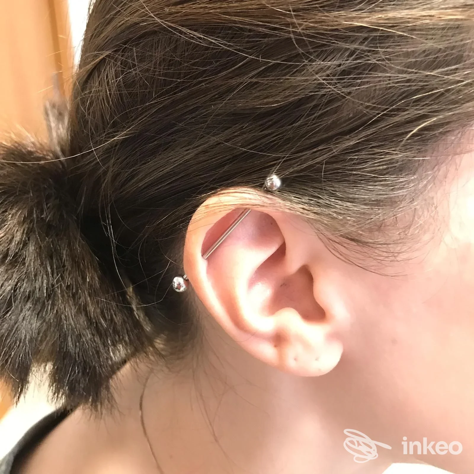 Primo piano di un piercing industrial sull'orecchio destro, barretta metallica visibile; LaGrange Tattoo, Musano.