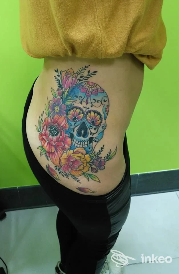 Grande tatuaggio colorato a forma di teschio decorato con fiori sul fianco; immagine inviata da Old Ink Tattoo Studio, Rovigo.