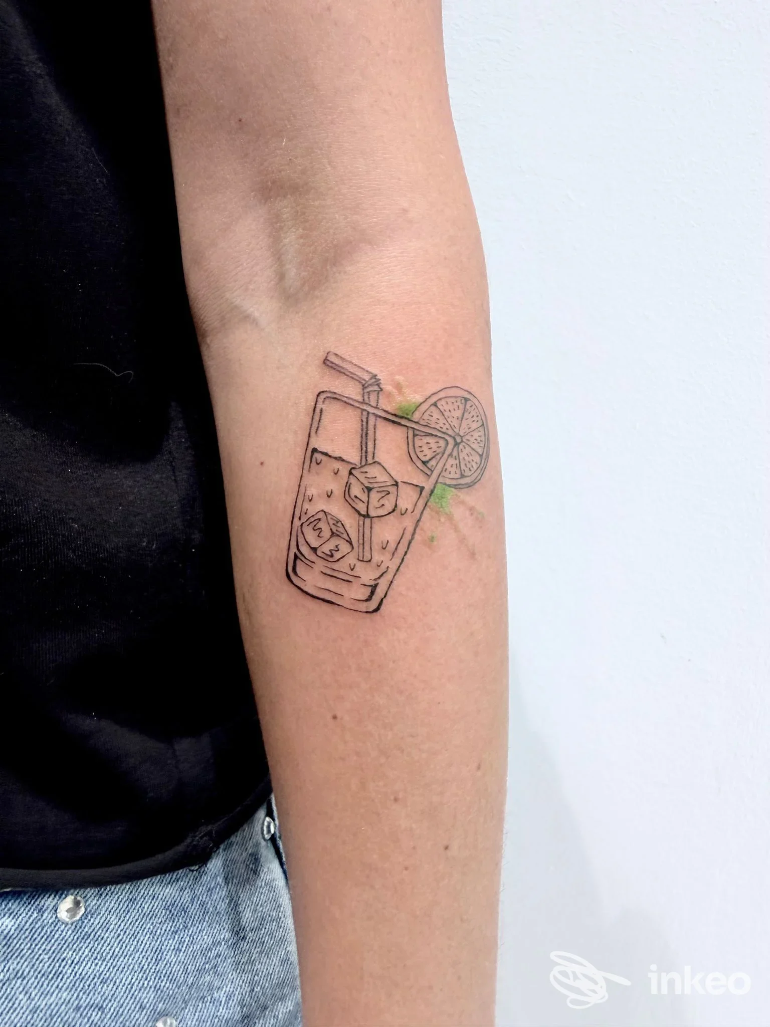Tatuaggio delicato sull'avambraccio di un bicchiere con cubetti di ghiaccio, cannuccia e fetta di lime, eseguito con linee sottili da Studio53 tattoo shop a Codiverno.