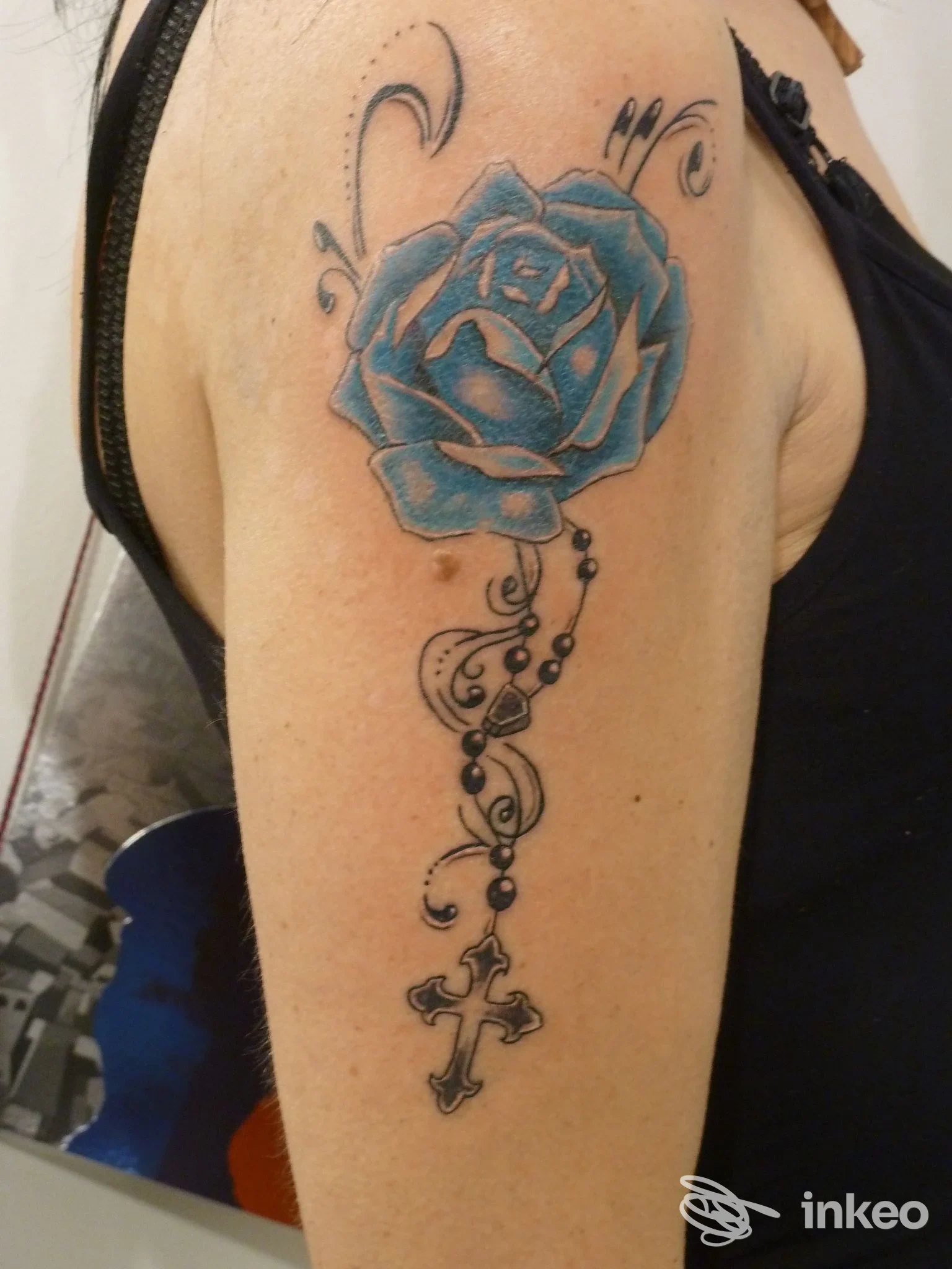Tatuaggio a rosa blu con ornamenti e croce sul braccio superiore, foto fornita da Tattoo'S Power a Peschiera del Garda.