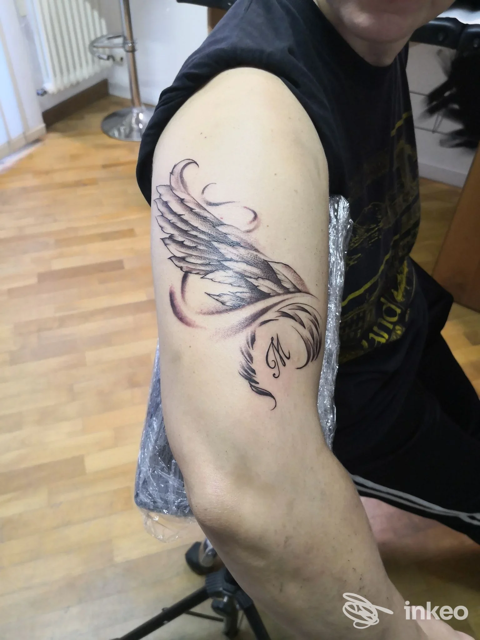 Primo piano di un tatuaggio a forma d'ala con iniziale sull'omero di un cliente, scattato nello studio Tattoo Smashed a Lancenigo.