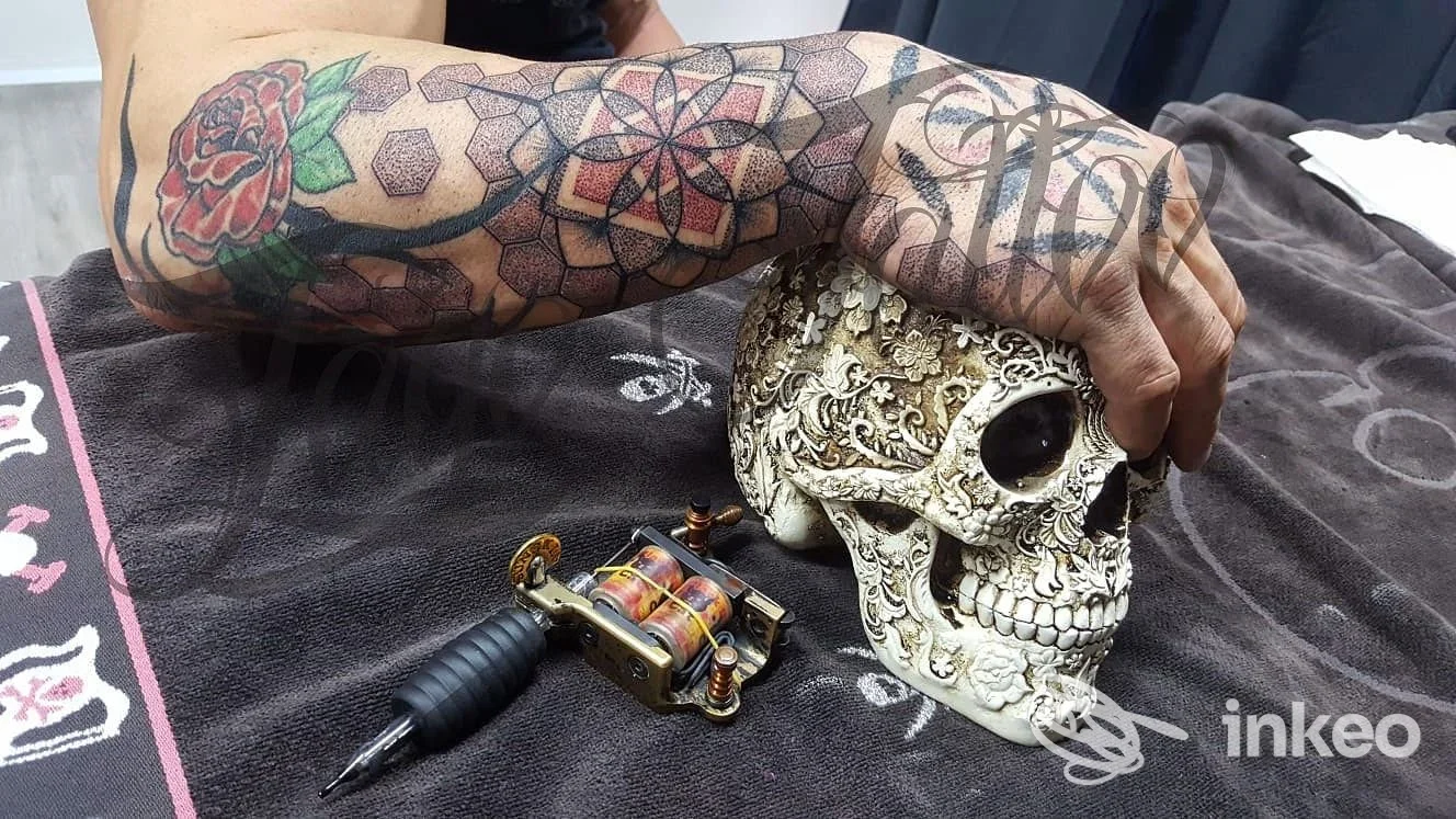 Braccio e mano tatuati con rose e motivi geometrici, mano che tiene un teschio decorativo — Zago Tattoo, Vo'.
