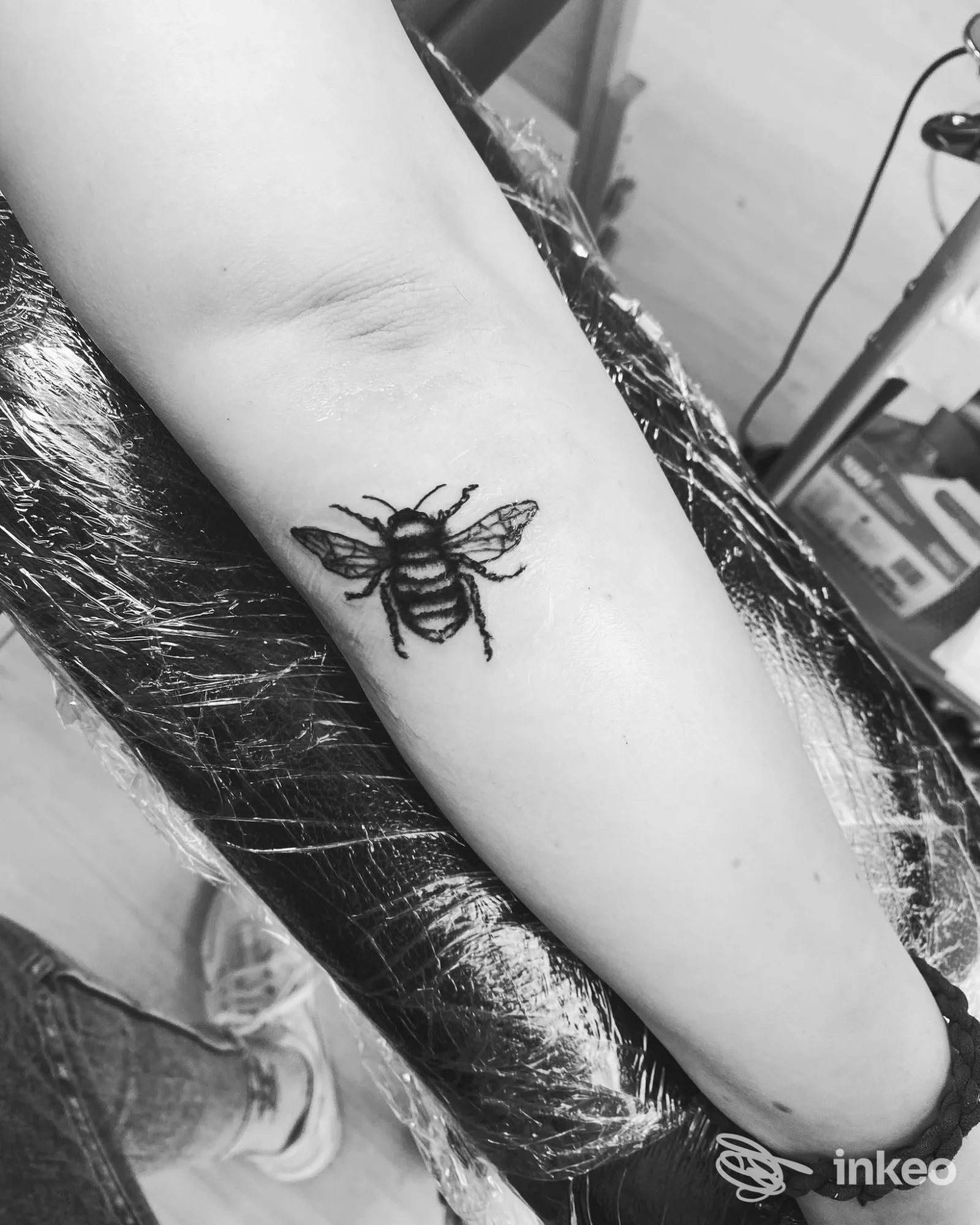 Tatuaggio su avambraccio: immagine in bianco e nero di una ape stilizzata in nero impressa sulla pelle, senza volto visibile e senza elementi promozionali.