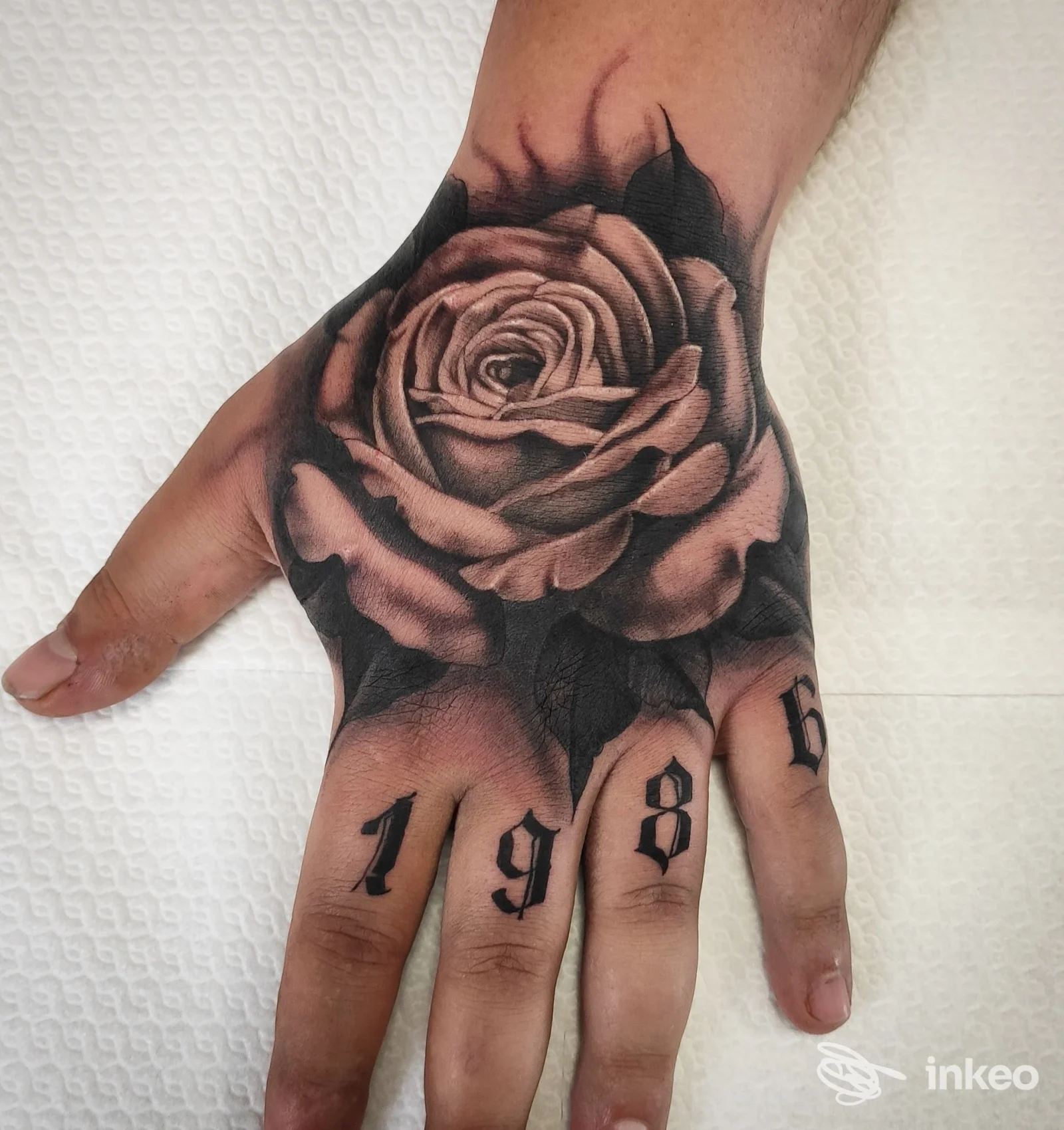 Tatuaggio realistico in bianco e nero di una rosa sul dorso della mano con numeri sulle dita. Atavic Tattoo, Rionero in Vulture.