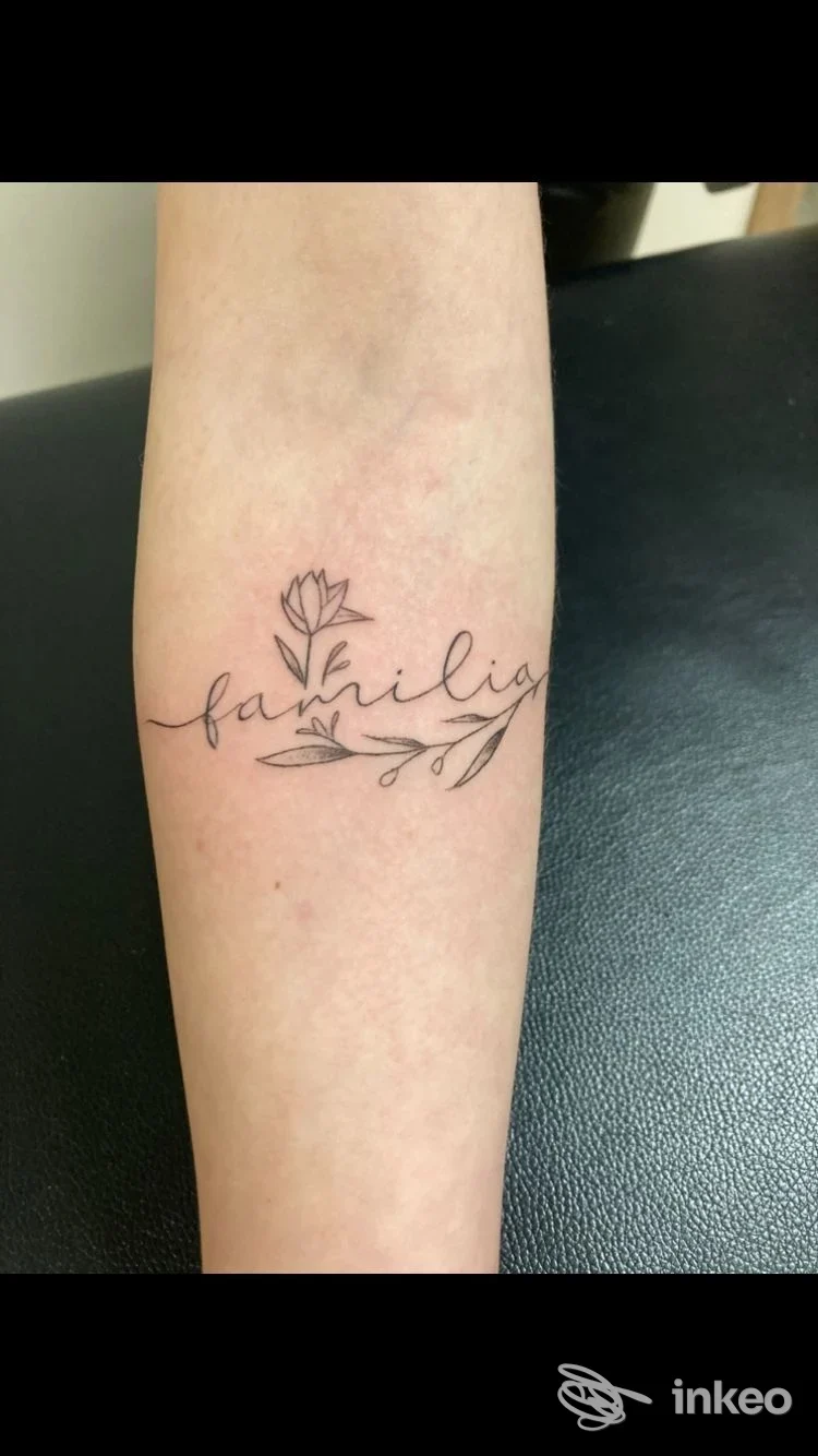 Tatuaggio fine line nero sull'avambraccio con scritta calligrafica e piccoli motivi floreali, foto di E.s. Tatto bodyart a Matera.