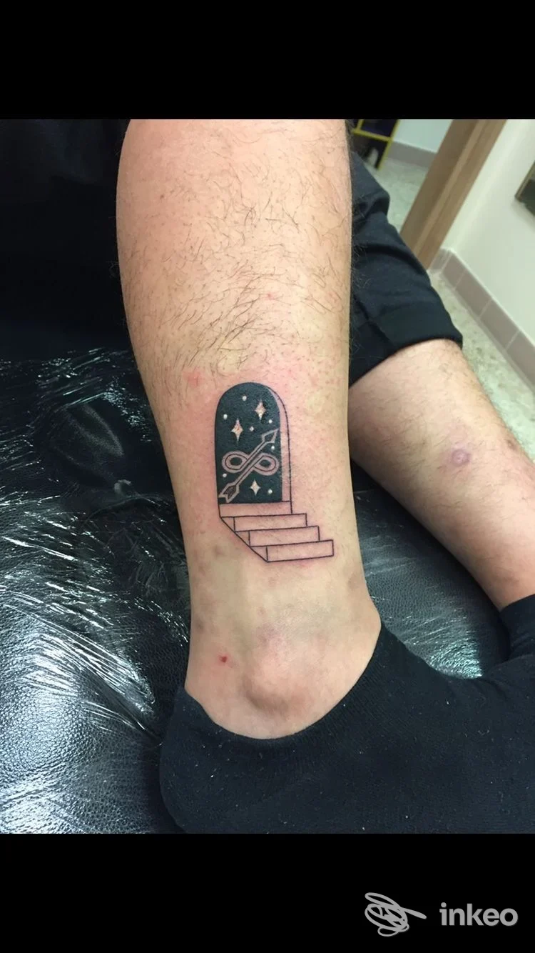 Tatuaggio a inchiostro nero con porta ad arco e gradini sulla caviglia, eseguito da E.s. Tatto bodyart a Matera.