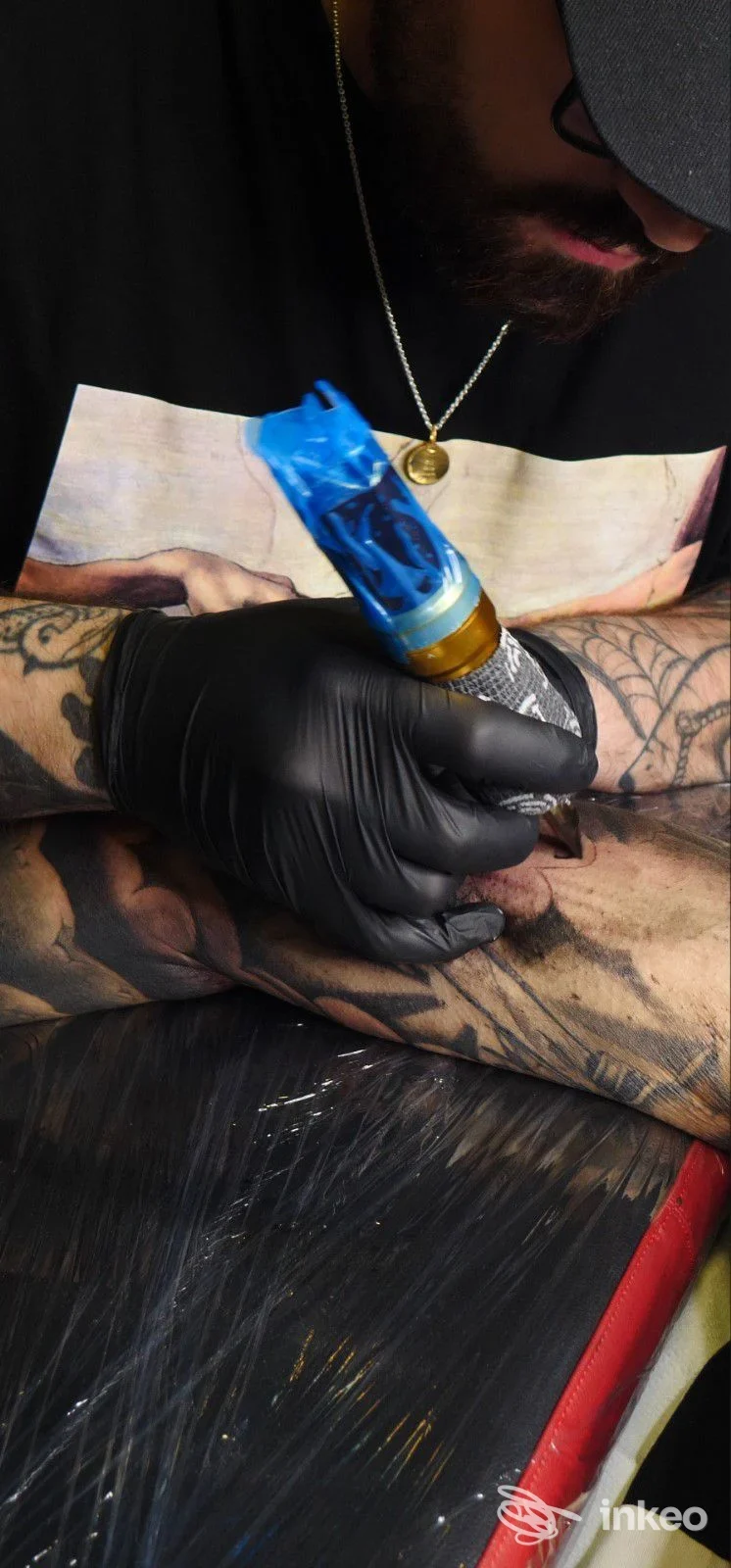 Primo piano del tatuatore che lavora sull'avambraccio con macchinetta avvolta in nastro blu. ETROM TATTOO, Pignola.
