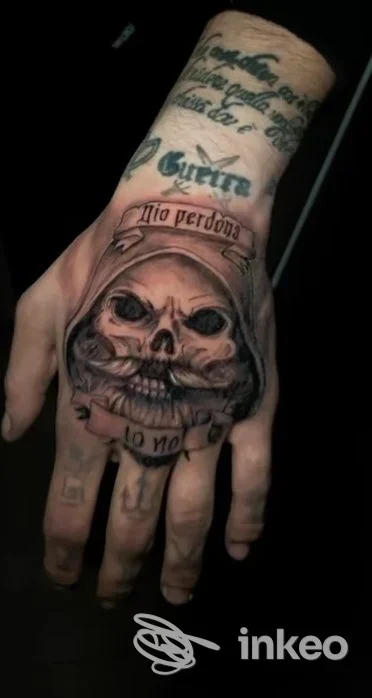 Primo piano del dorso di una mano tatuata con un grande teschio e scritte, foto fornita da ETROM TATTOO, Pignola.